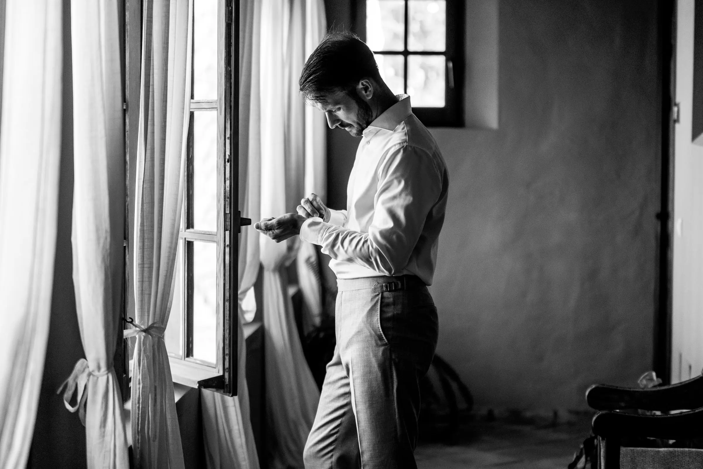 Black and white of the groom checking his cufflinks by a tall window, Hacienda San José, Mijas