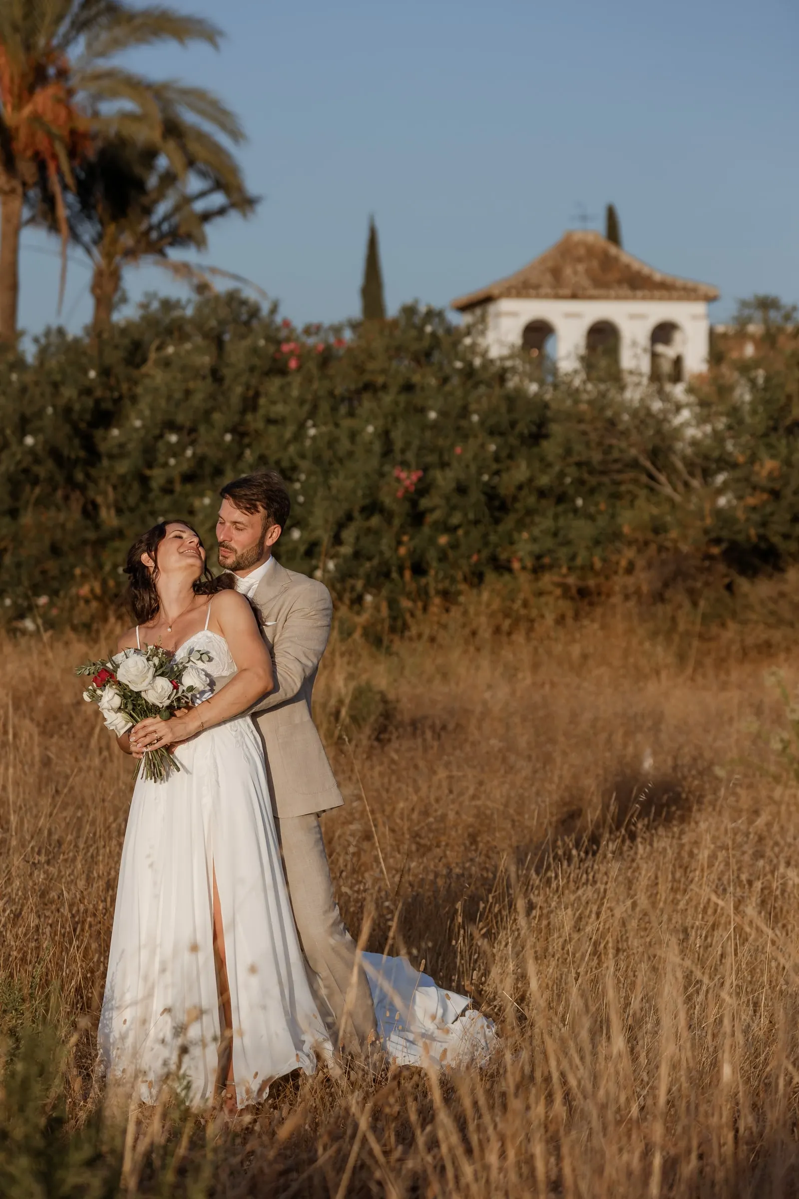 The couple embracing in tall golden grass with the bell tower behind, Hacienda San José, Mijas