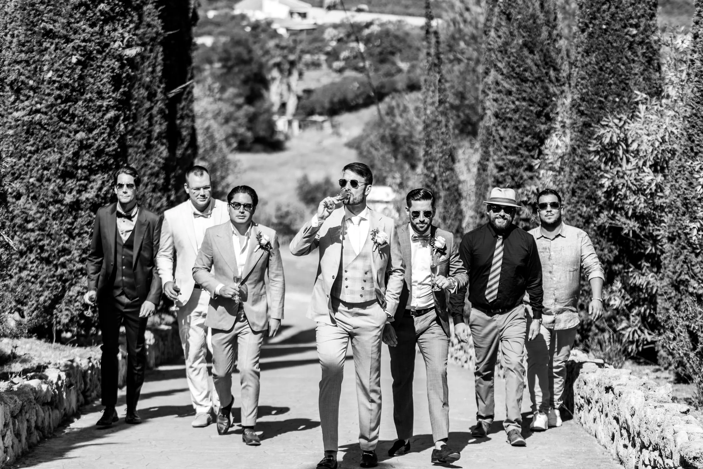 Black and white of the groom and friends walking up a tree-lined path in sunglasses, Hacienda San José, Mijas