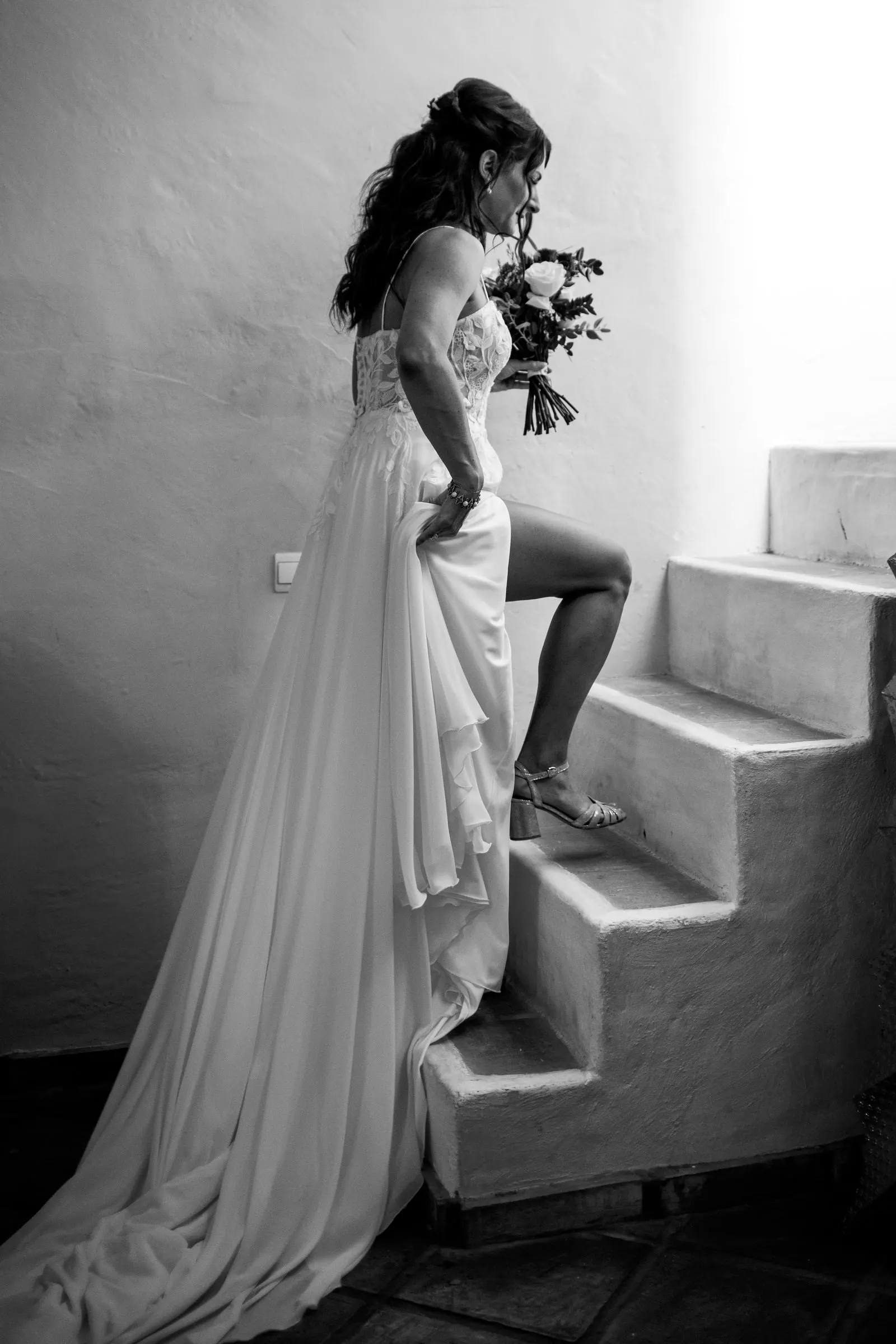 Black and white of the bride climbing white steps, smelling her bouquet, Hacienda San José, Mijas