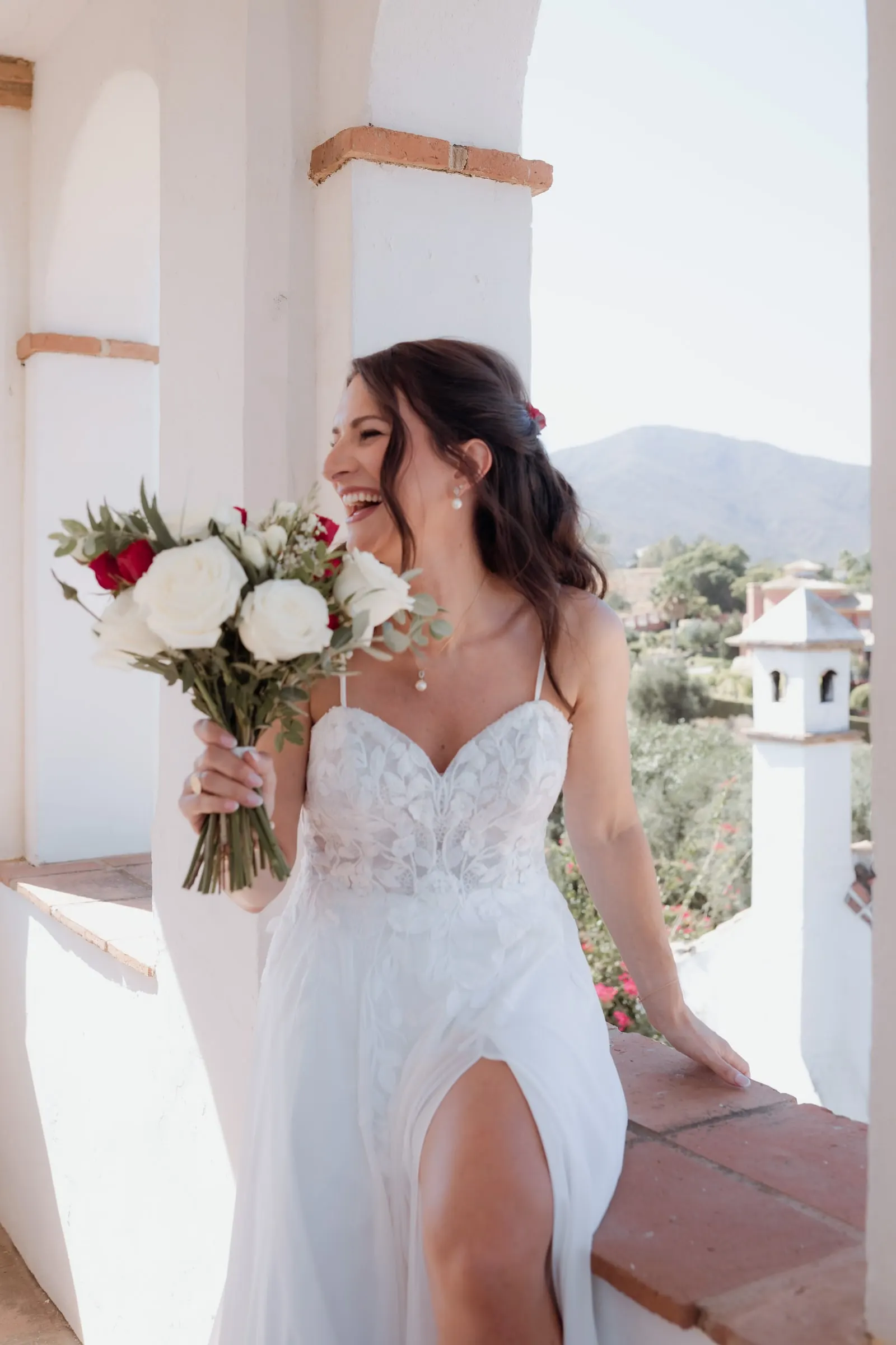 The bride laughing on a sunny whitewashed balcony with the hills behind her, Hacienda San José, Mijas