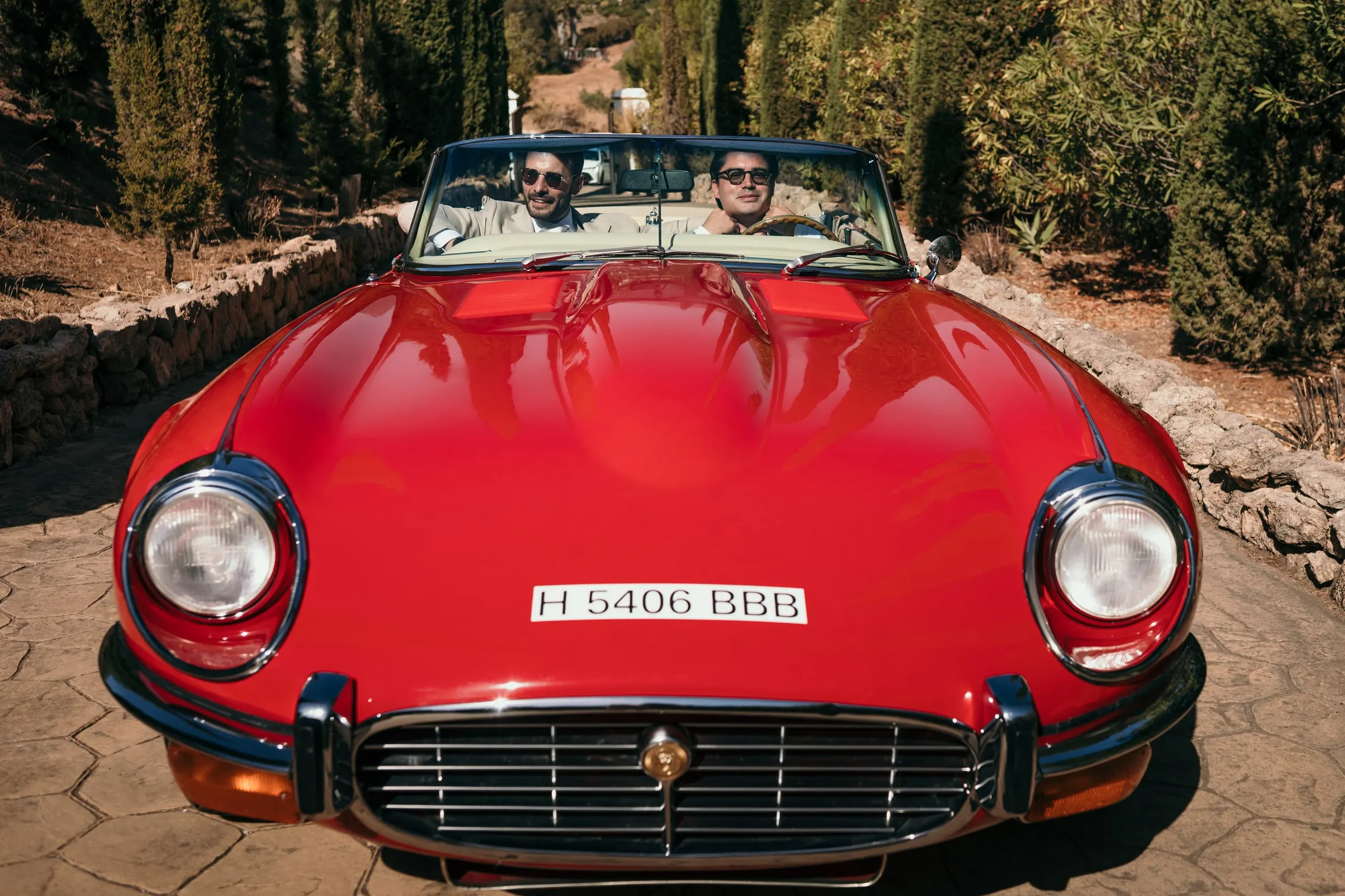 Two men driving a red vintage convertible up a cobbled drive, front view, Hacienda San José, Mijas