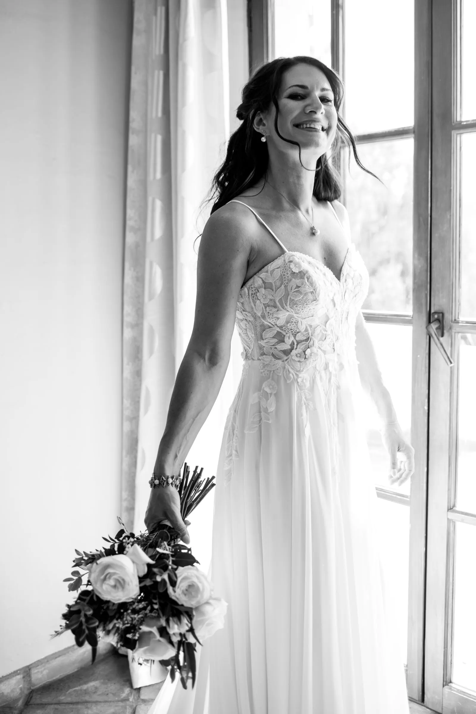 Black and white of the bride smiling by an open window, bouquet held low, Hacienda San José, Mijas