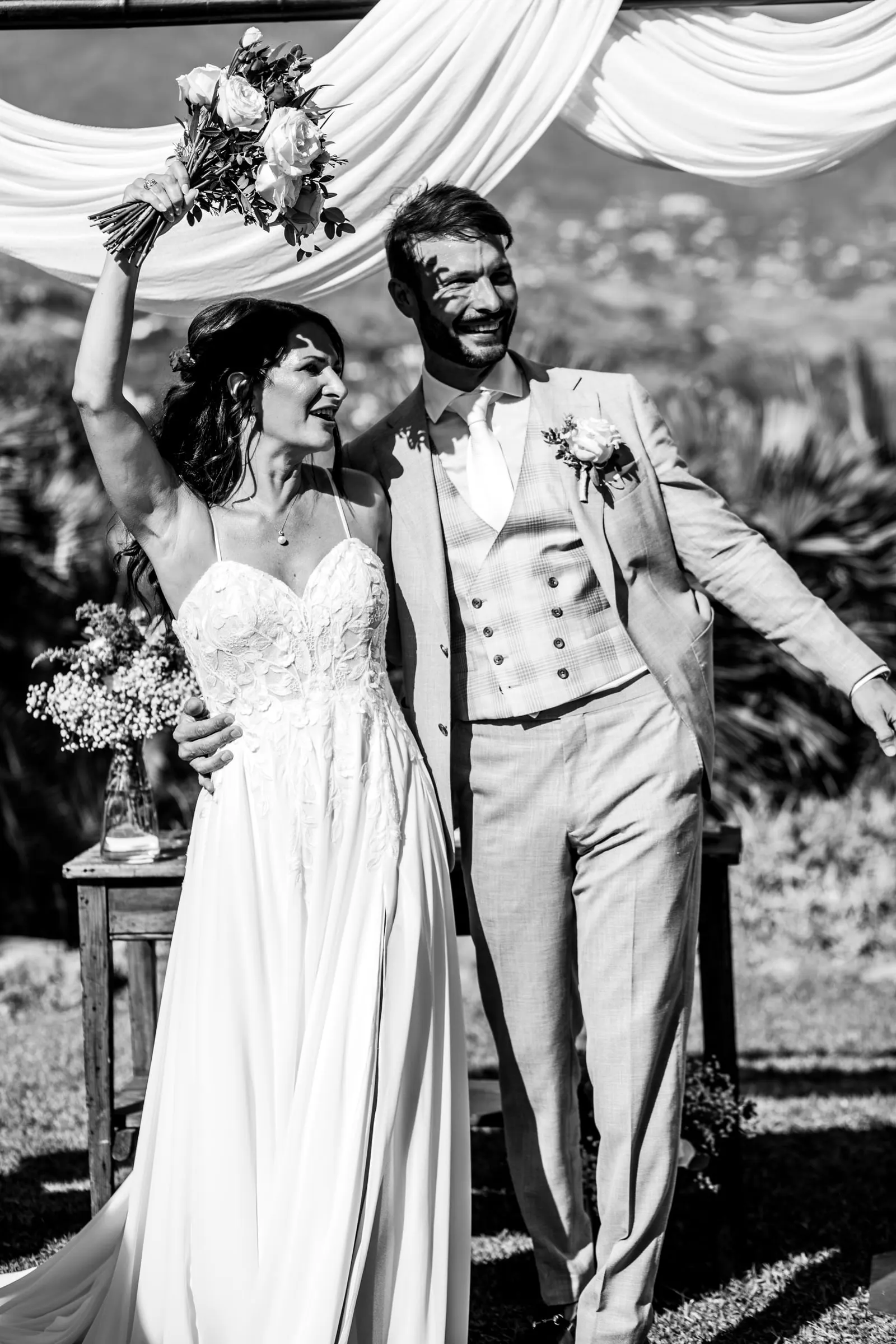 Black and white of the newlyweds cheering by the canopy, bouquet raised high, Hacienda San José, Mijas