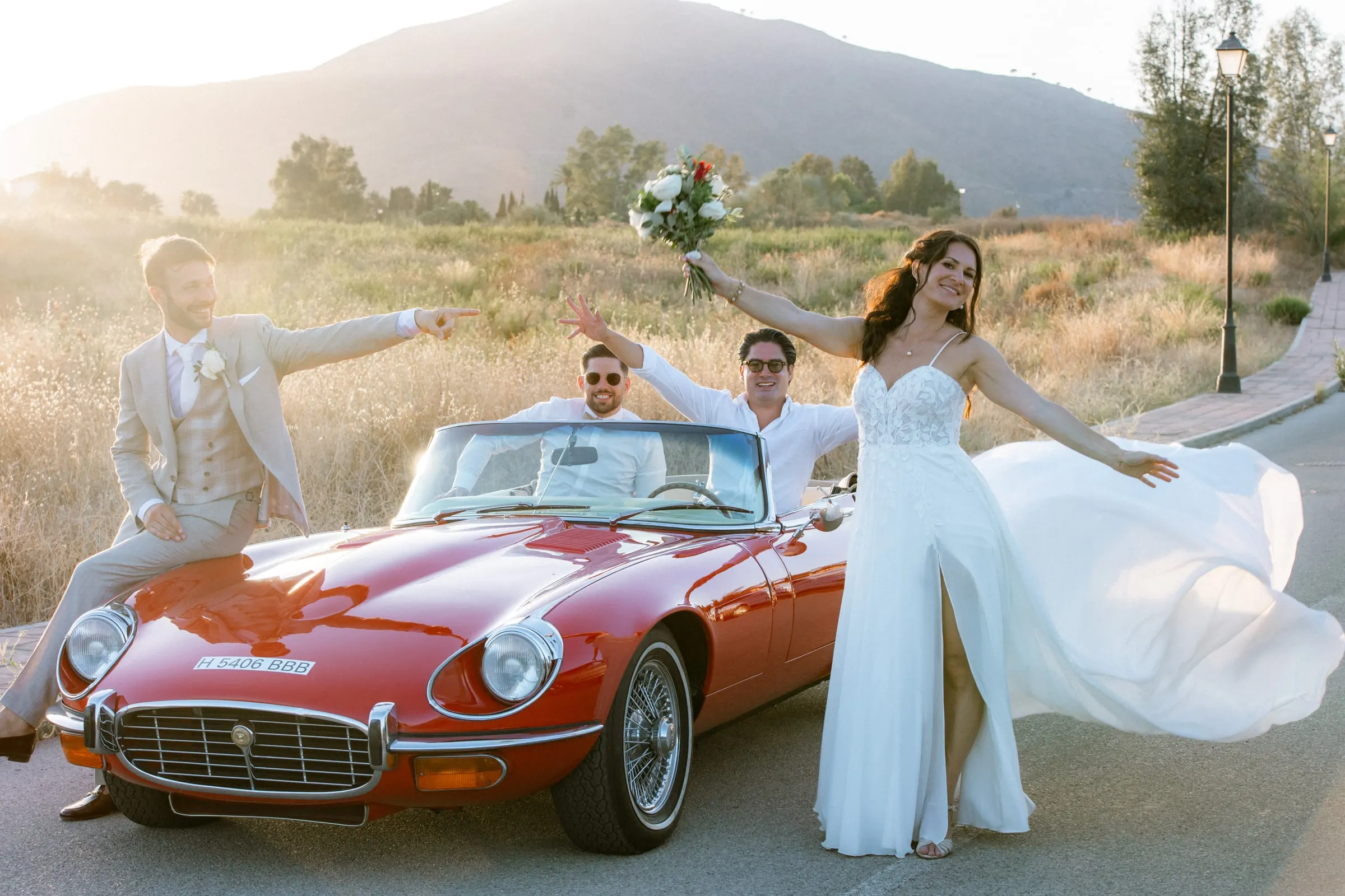 The couple and friends cheering around a red vintage convertible in the late sun, Hacienda San José, Mijas