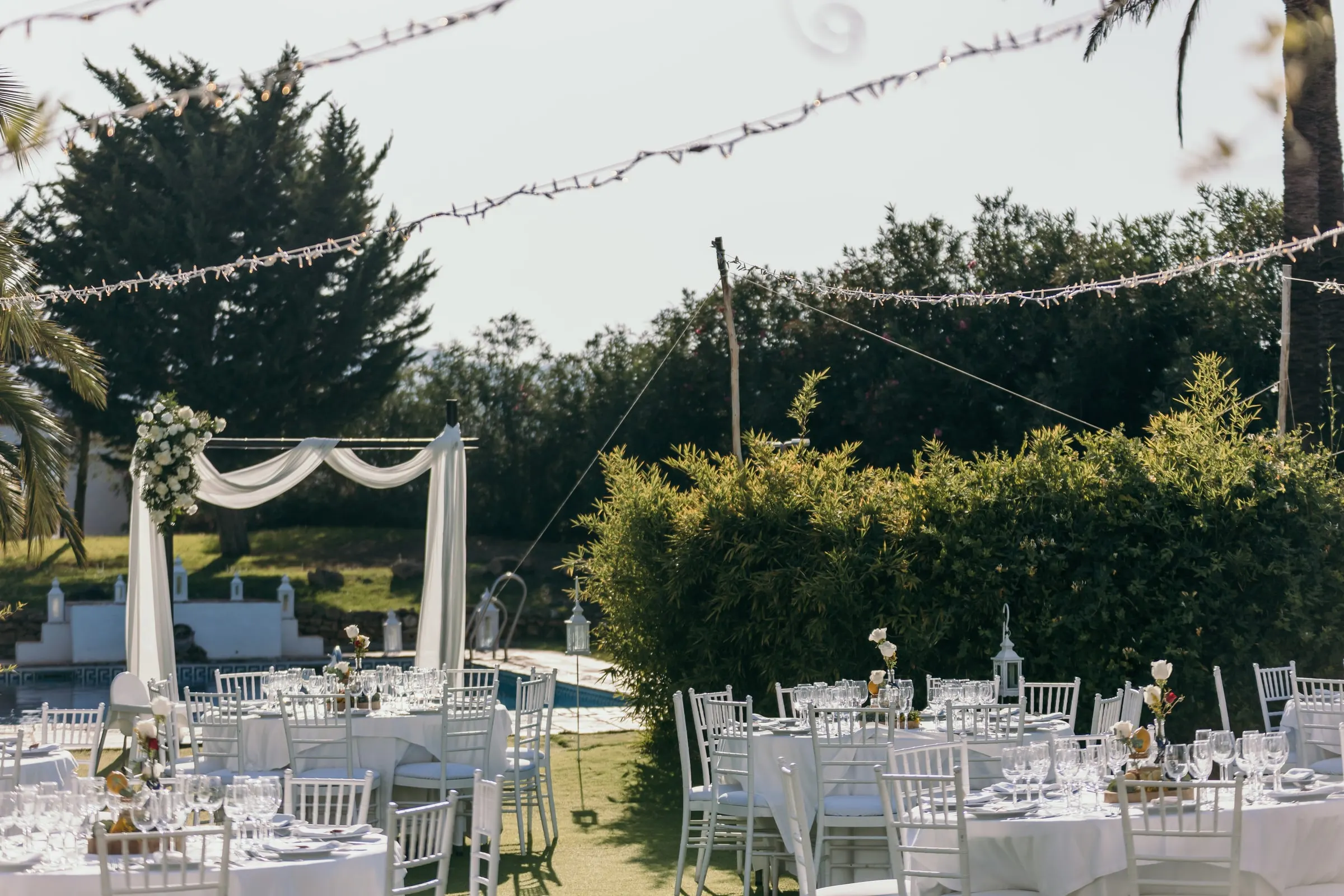 Round tables set on the lawn under strings of lights, with the canopy and pool behind, Hacienda San José, Mijas