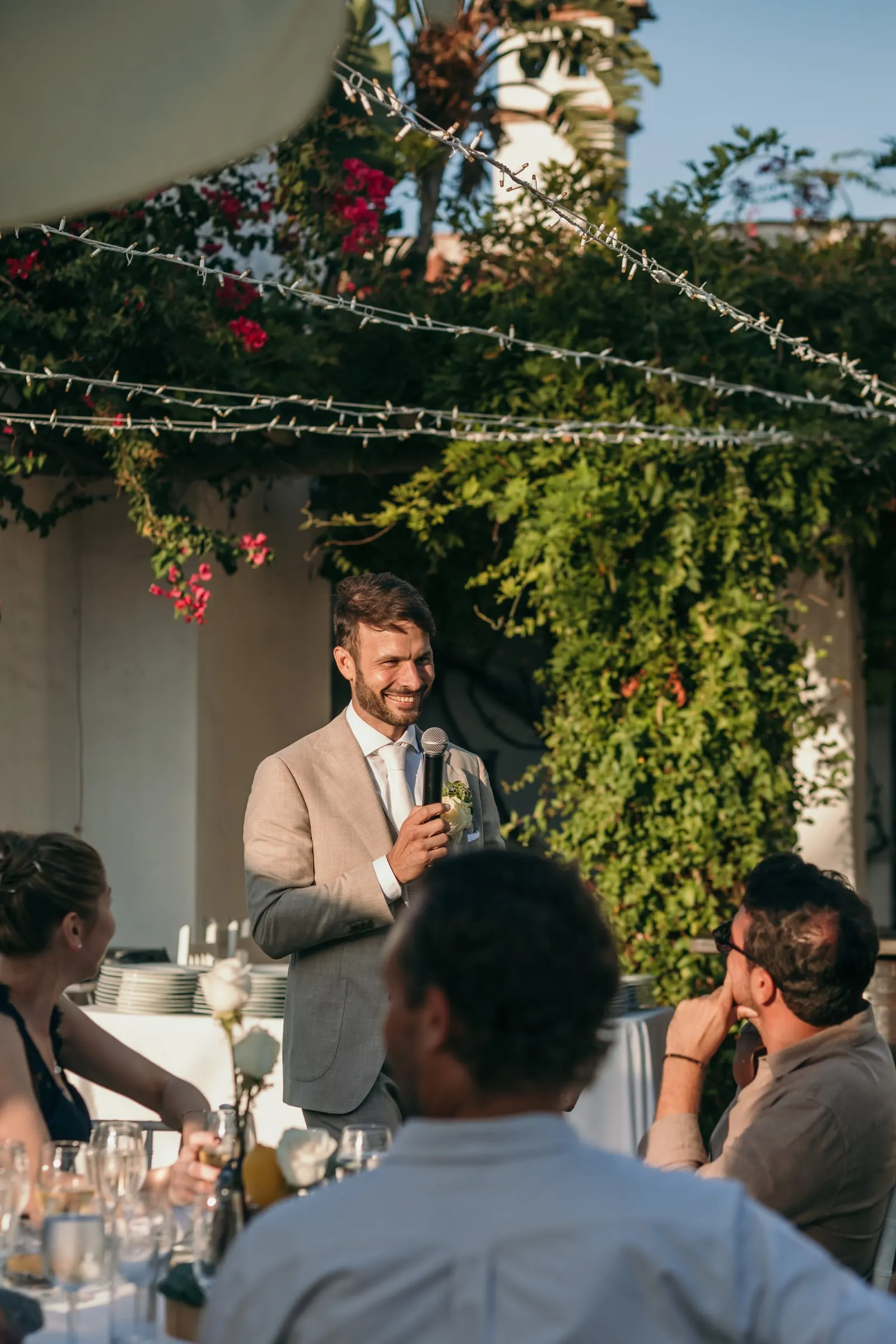 The groom giving a speech under bougainvillea as guests listen at their tables, Hacienda San José, Mijas