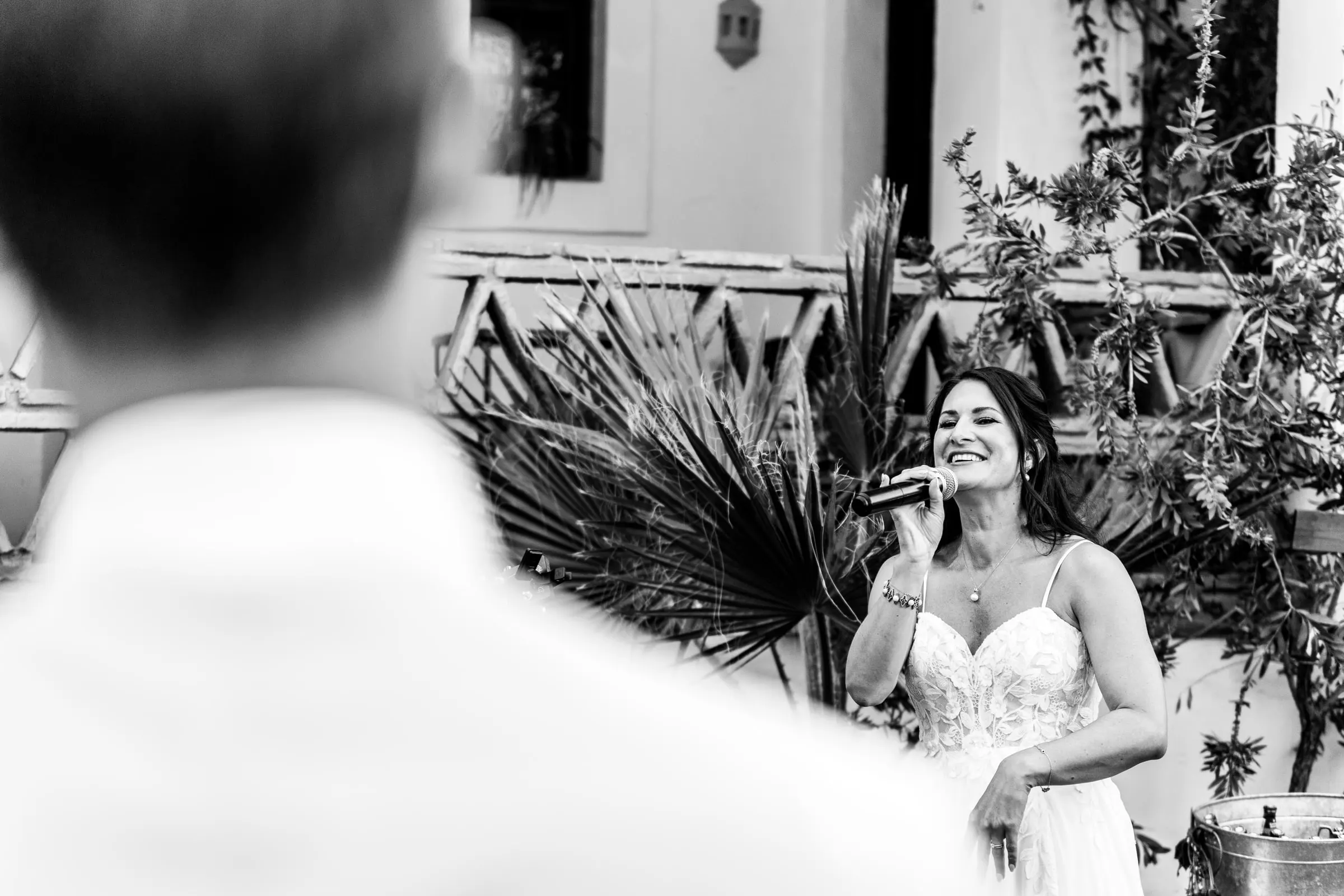 Black and white of the bride singing into a microphone in front of palm leaves, Hacienda San José, Mijas