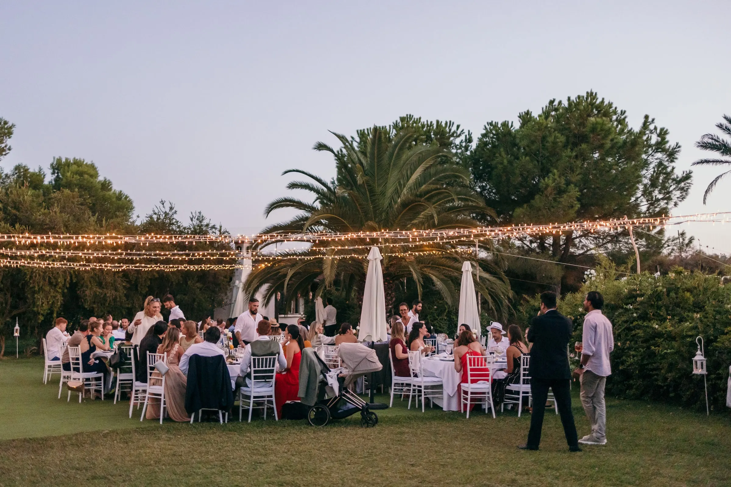 Guests at dinner on the lawn under fairy lights and palm trees at dusk, Hacienda San José, Mijas