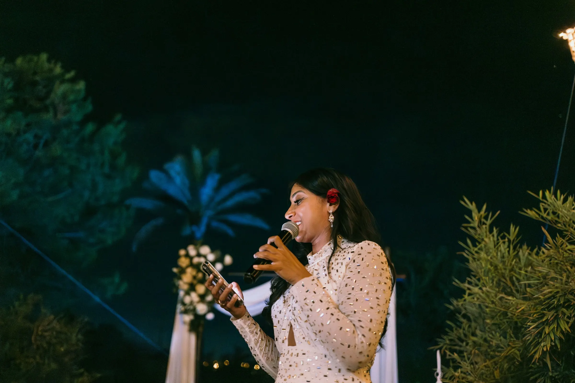 A guest in a white dotted dress reading a speech into a microphone at night, Hacienda San José, Mijas