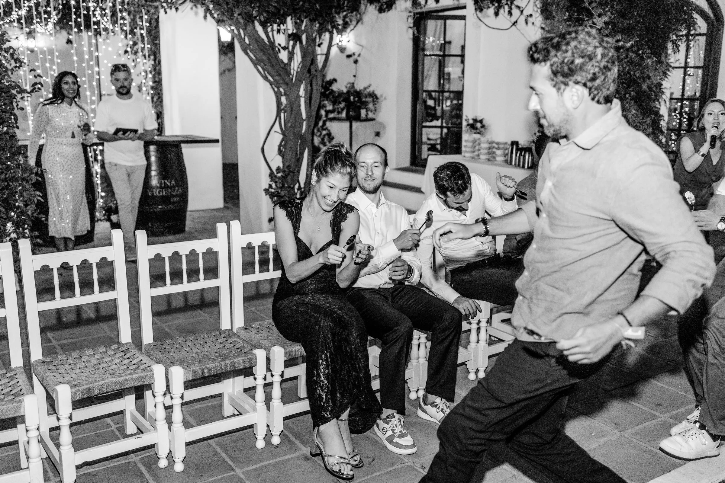 Black and white of a guest dancing past friends seated on white chairs, Hacienda San José, Mijas