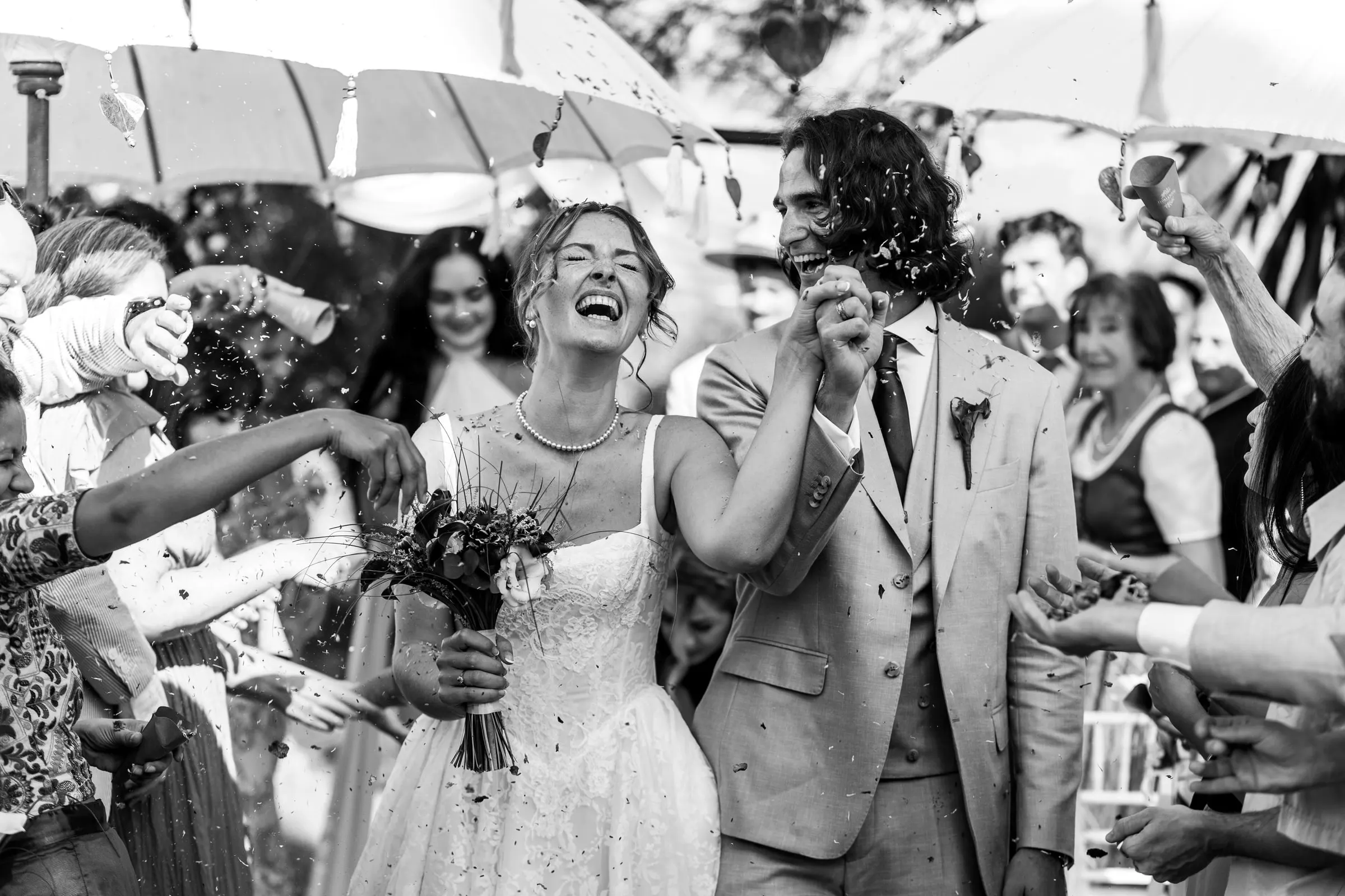 Black and white of the newlyweds laughing as guests shower them with confetti, Hacienda San José, Mijas