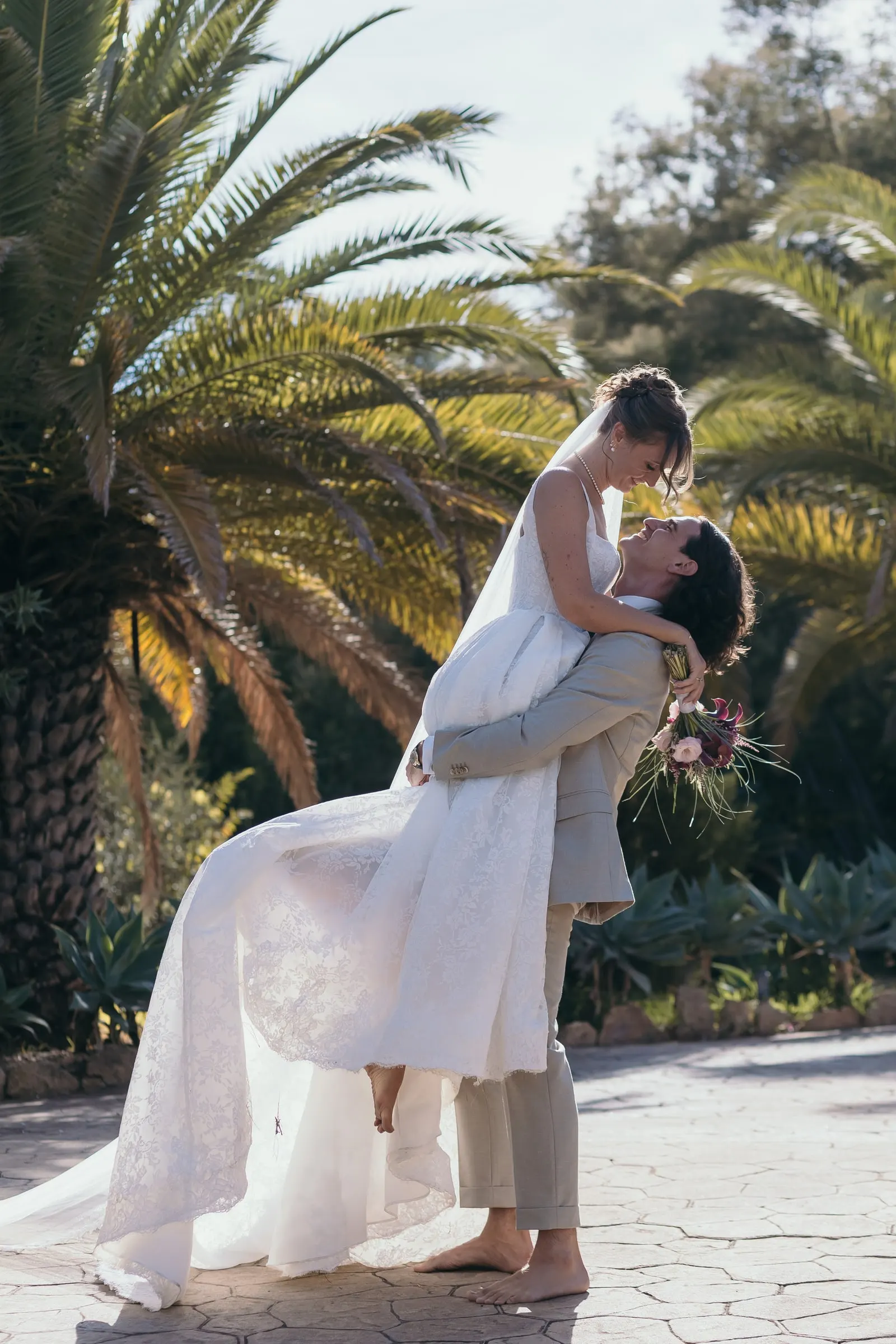 The groom lifting the bride into a kiss beneath tall palm trees, Hacienda San José, Mijas