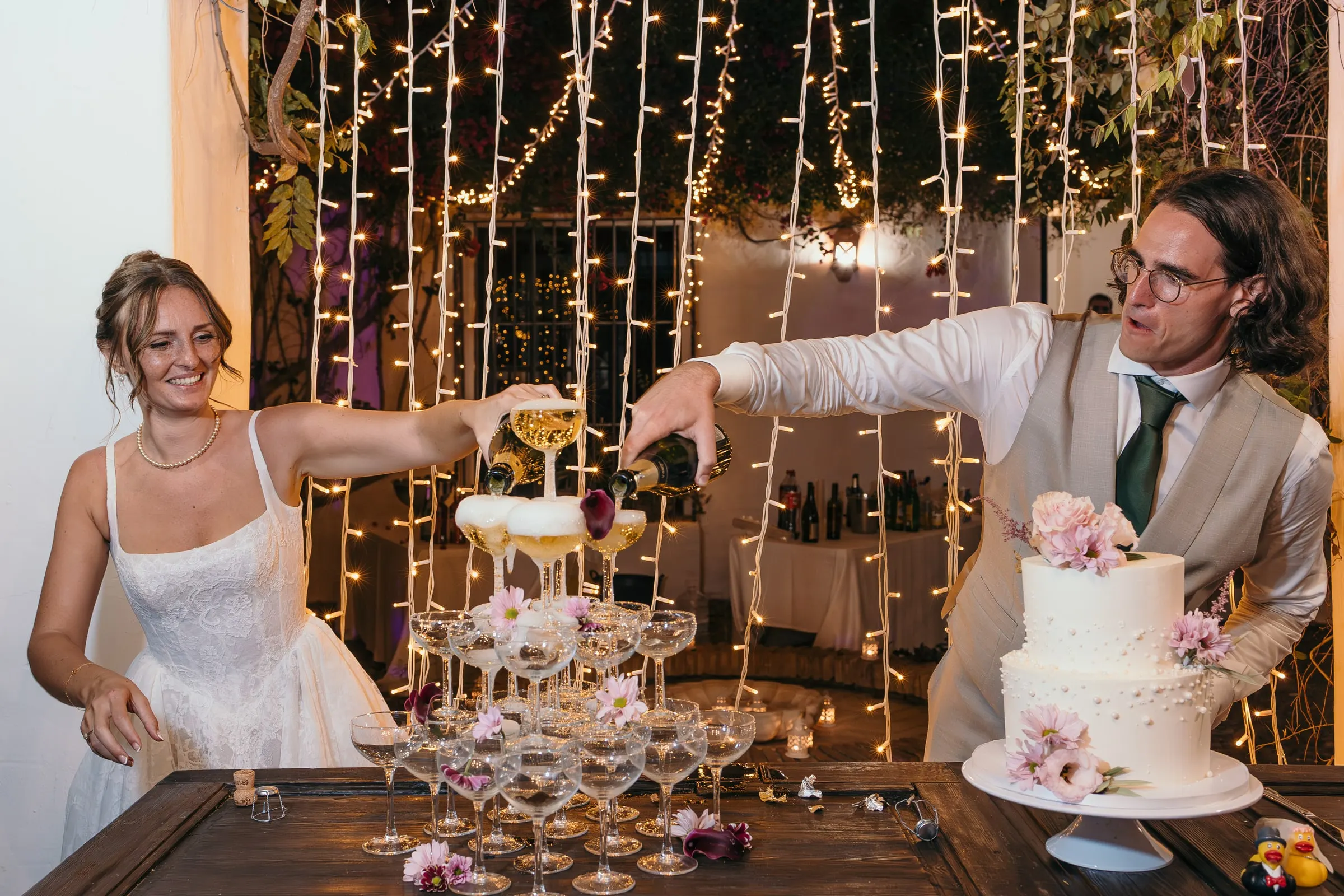 Bride and groom pouring champagne into a coupe tower next to their wedding cake at Hacienda San José, Mijas