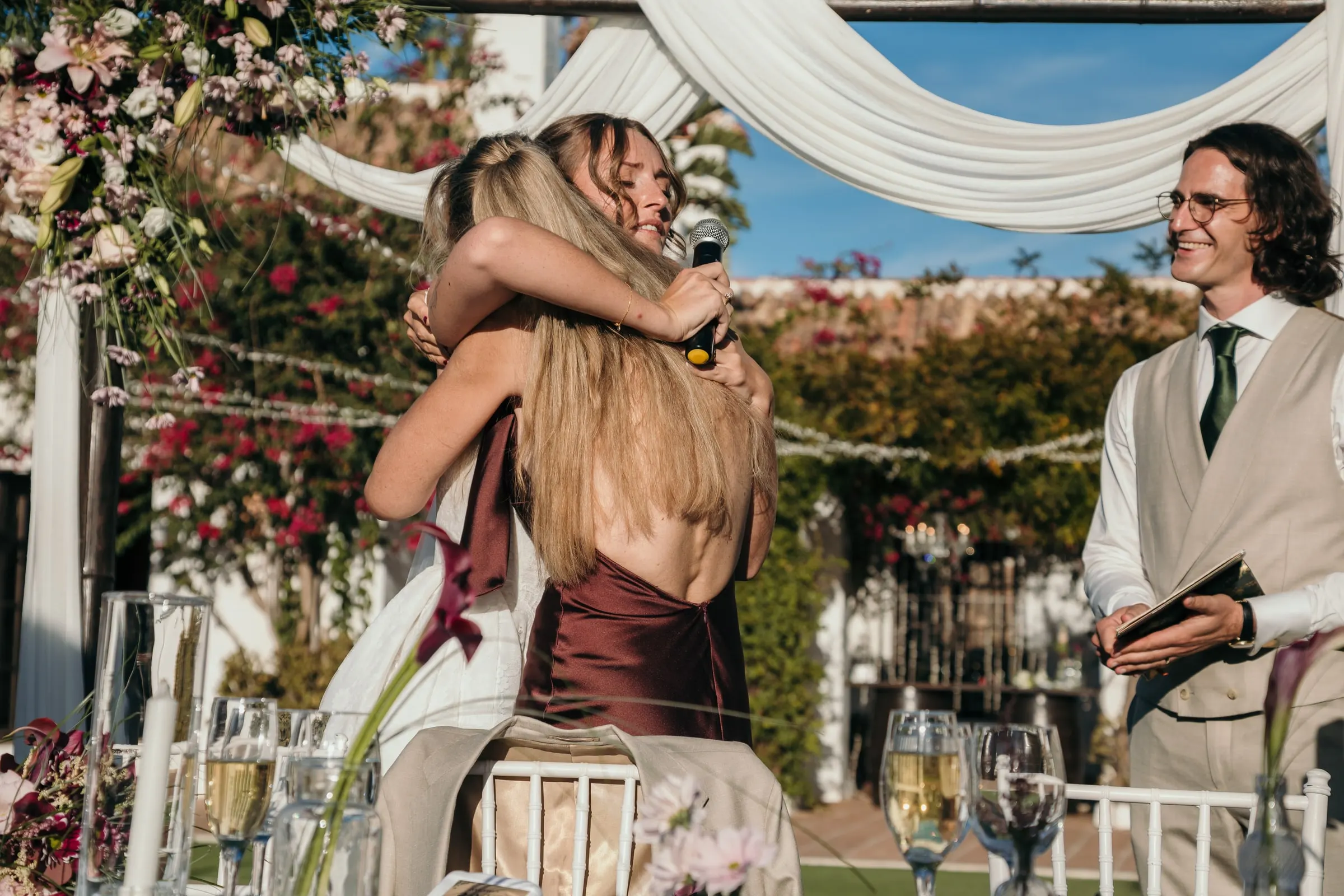 The bride hugging a guest who has just given a speech, the groom smiling beside, Hacienda San José, Mijas