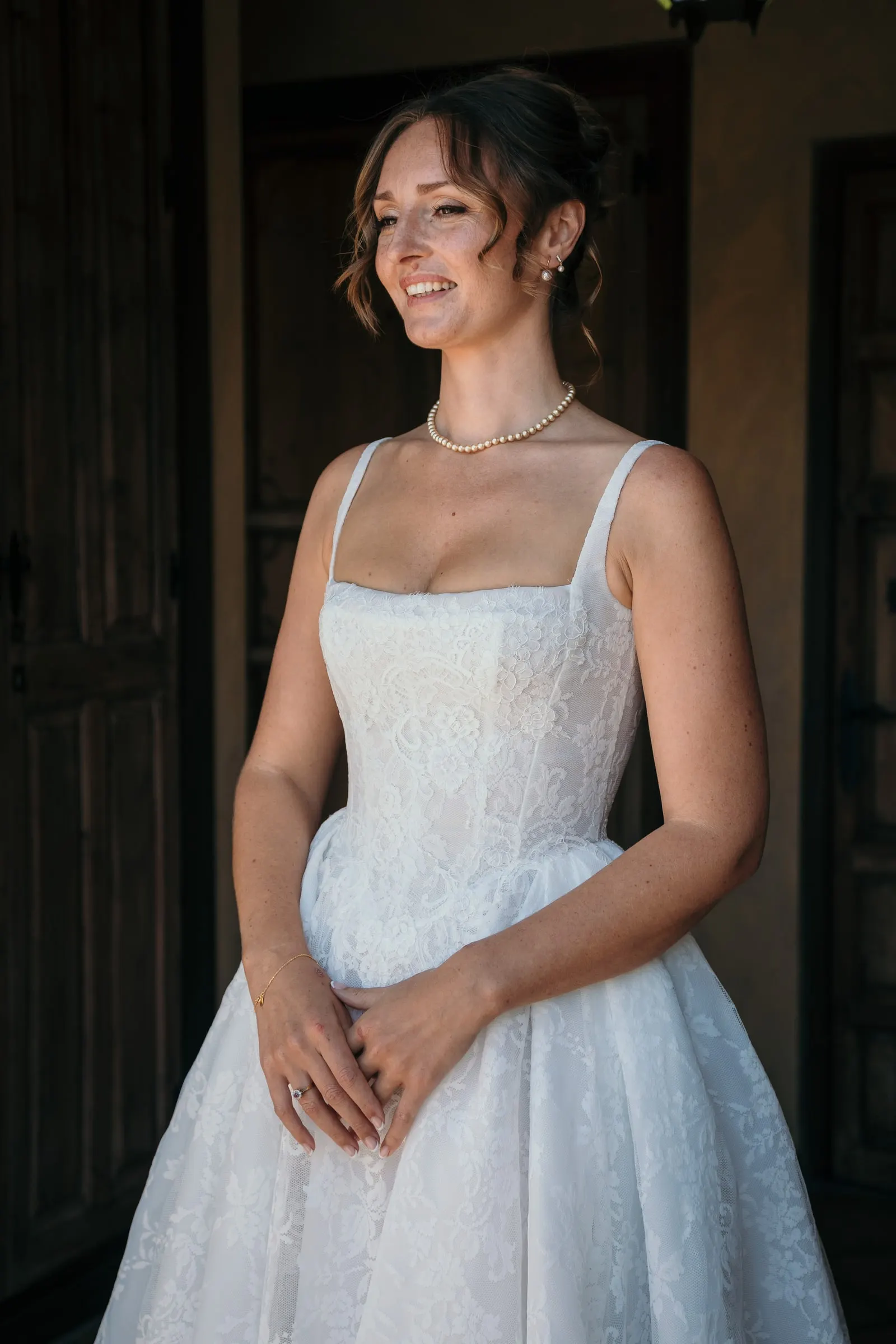 The bride smiling in a dark doorway, hands folded, in her pearl necklace, Hacienda San José, Mijas