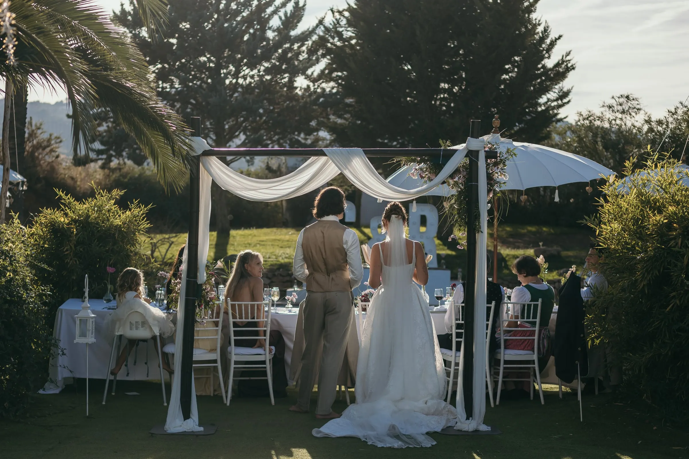 The ceremony under a draped canopy seen from behind the guests' chairs, Hacienda San José, Mijas