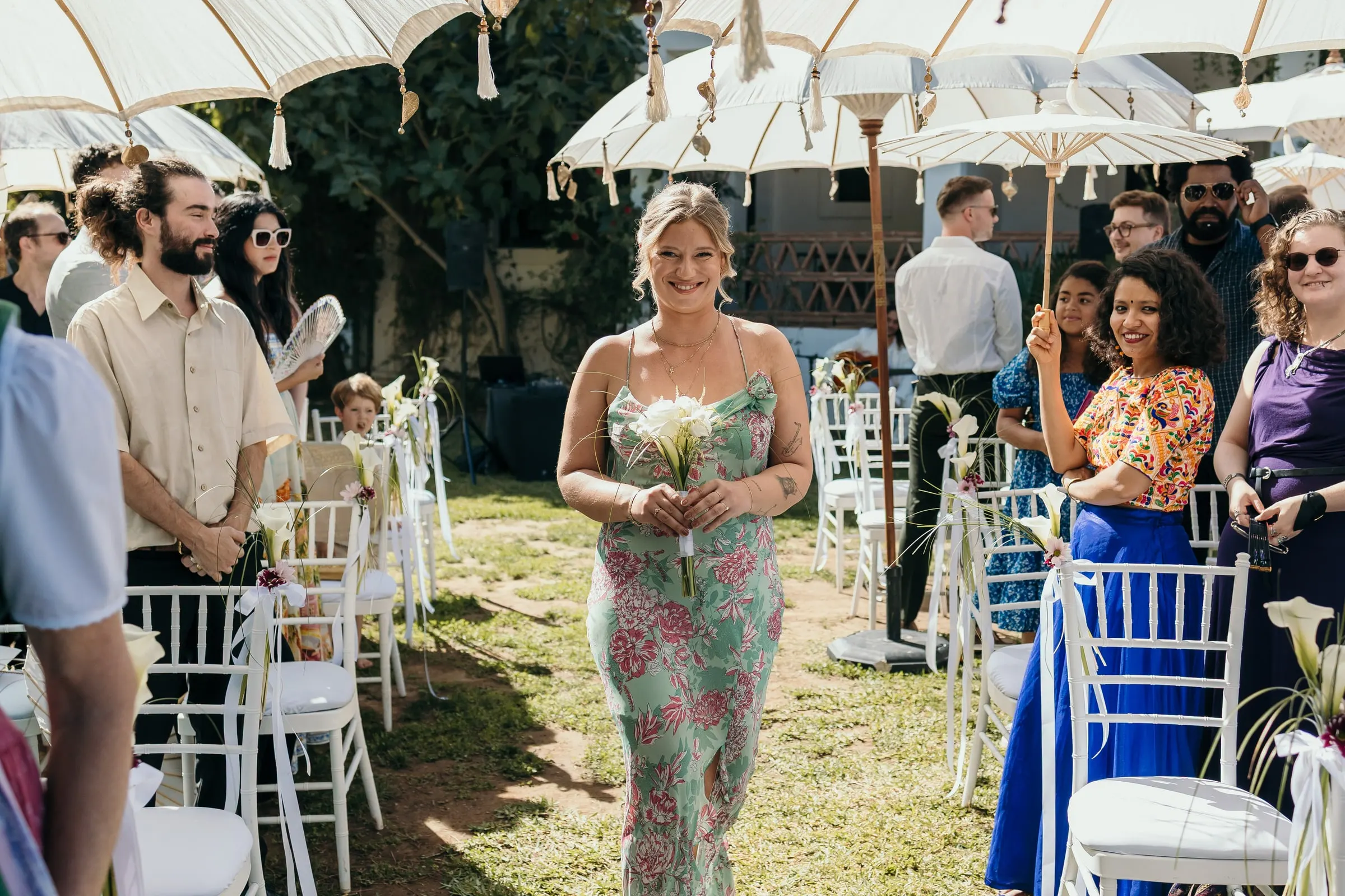 A guest in a floral dress walking down the aisle between chairs and parasols, Hacienda San José, Mijas