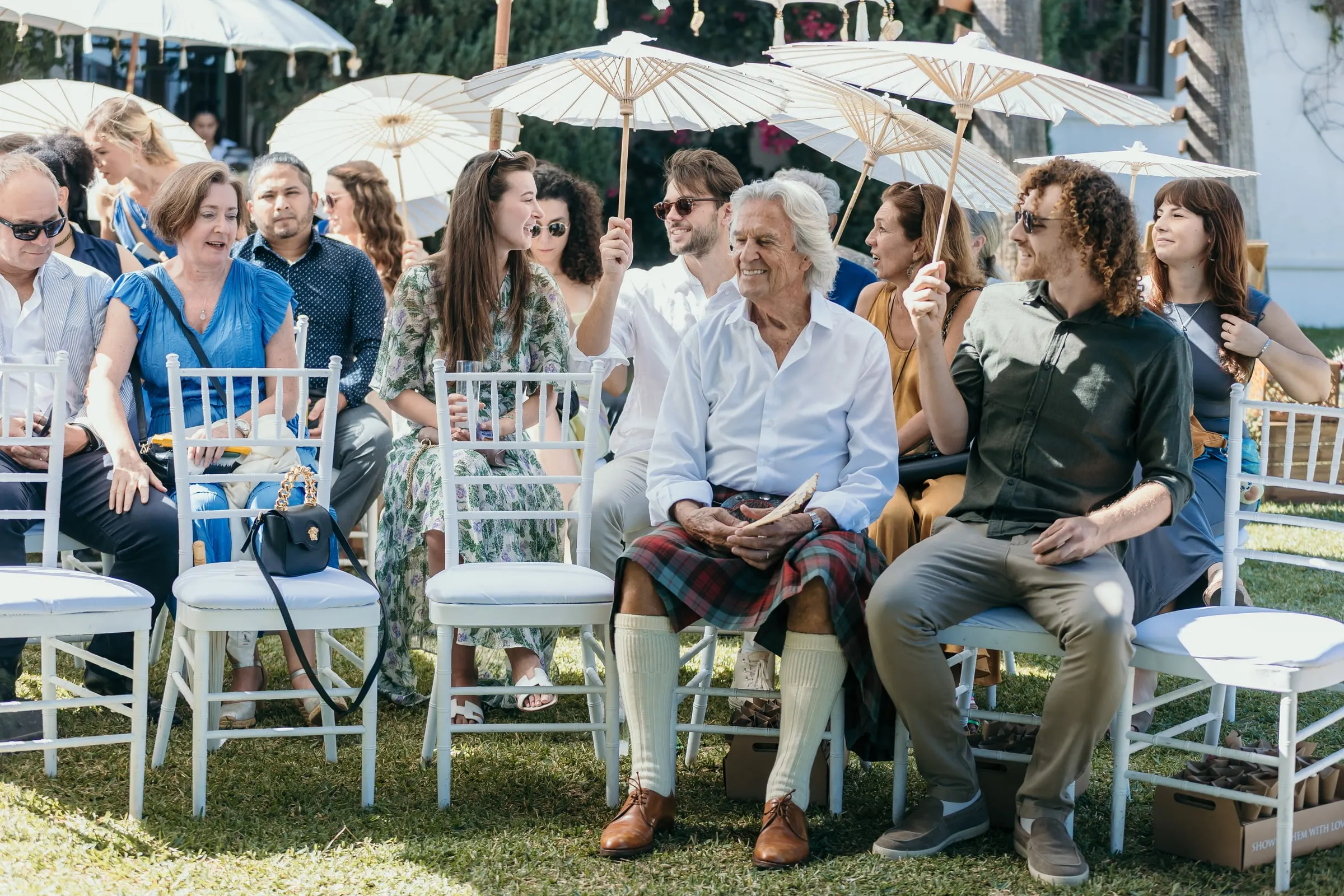 Guests seated under paper parasols at the ceremony, a man in a kilt in front, Hacienda San José, Mijas