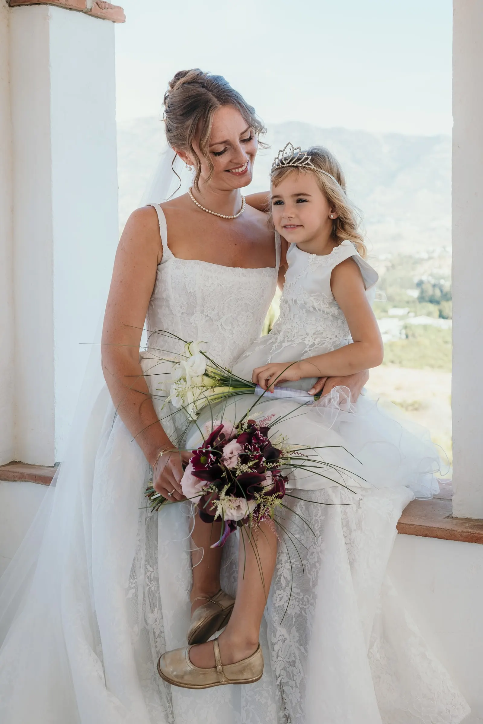 The bride sitting on a ledge with the flower girl on her knee, valley behind, Hacienda San José, Mijas