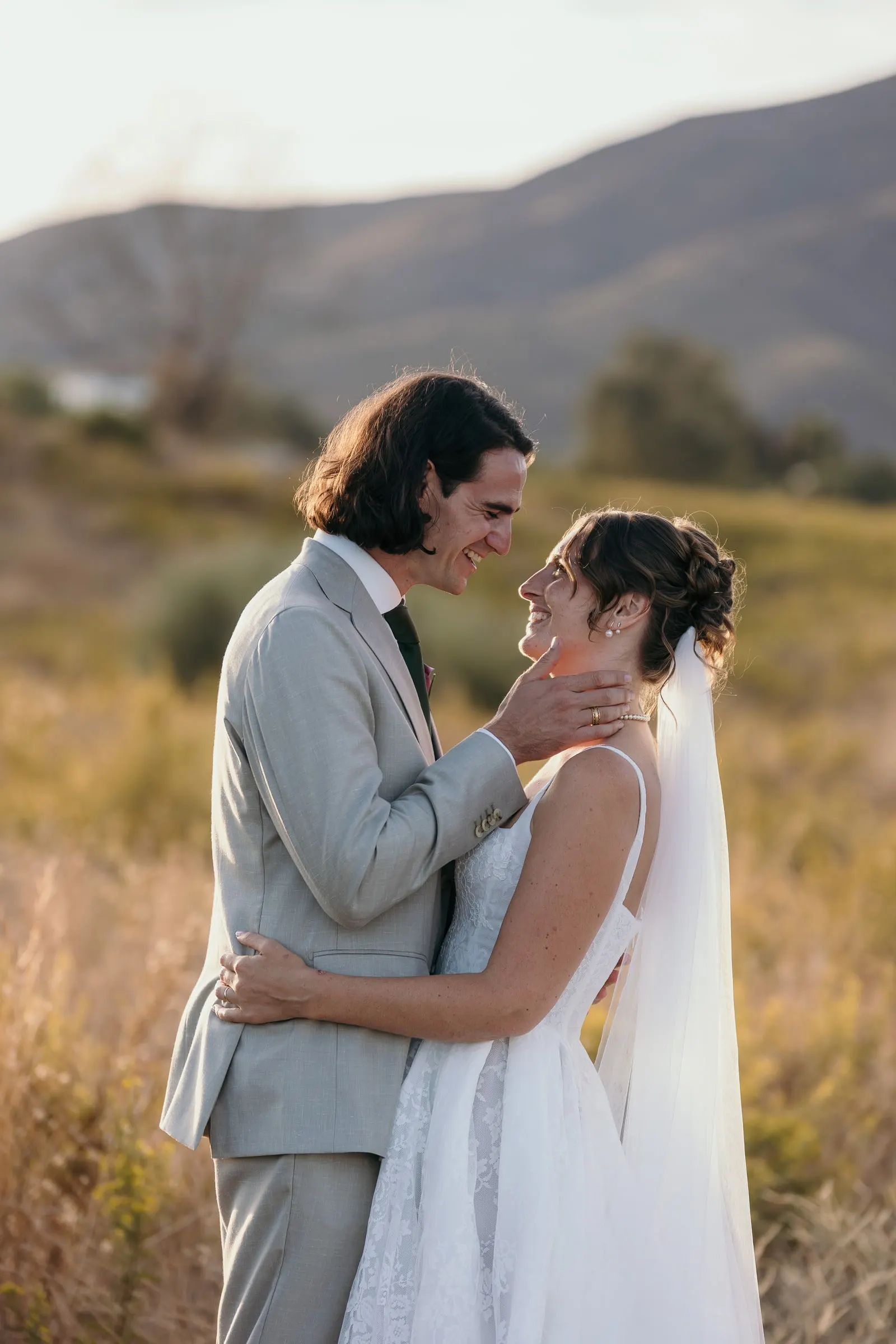 The groom cradling the bride's face in a golden field with the hills behind, Hacienda San José, Mijas
