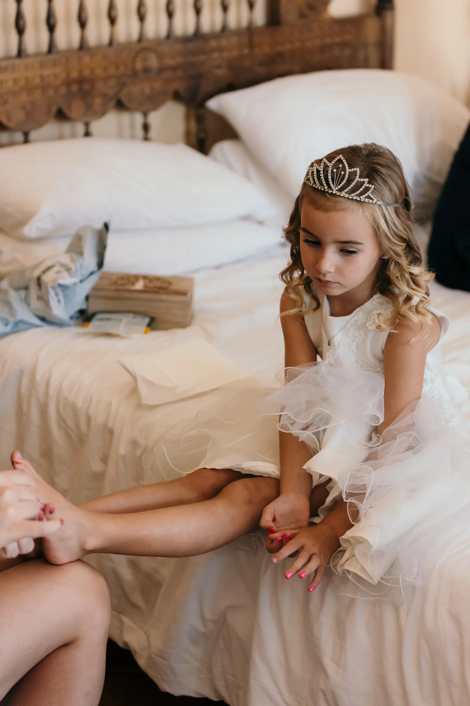 The flower girl in a tiara sitting on a bed as her nails are painted, Hacienda San José, Mijas