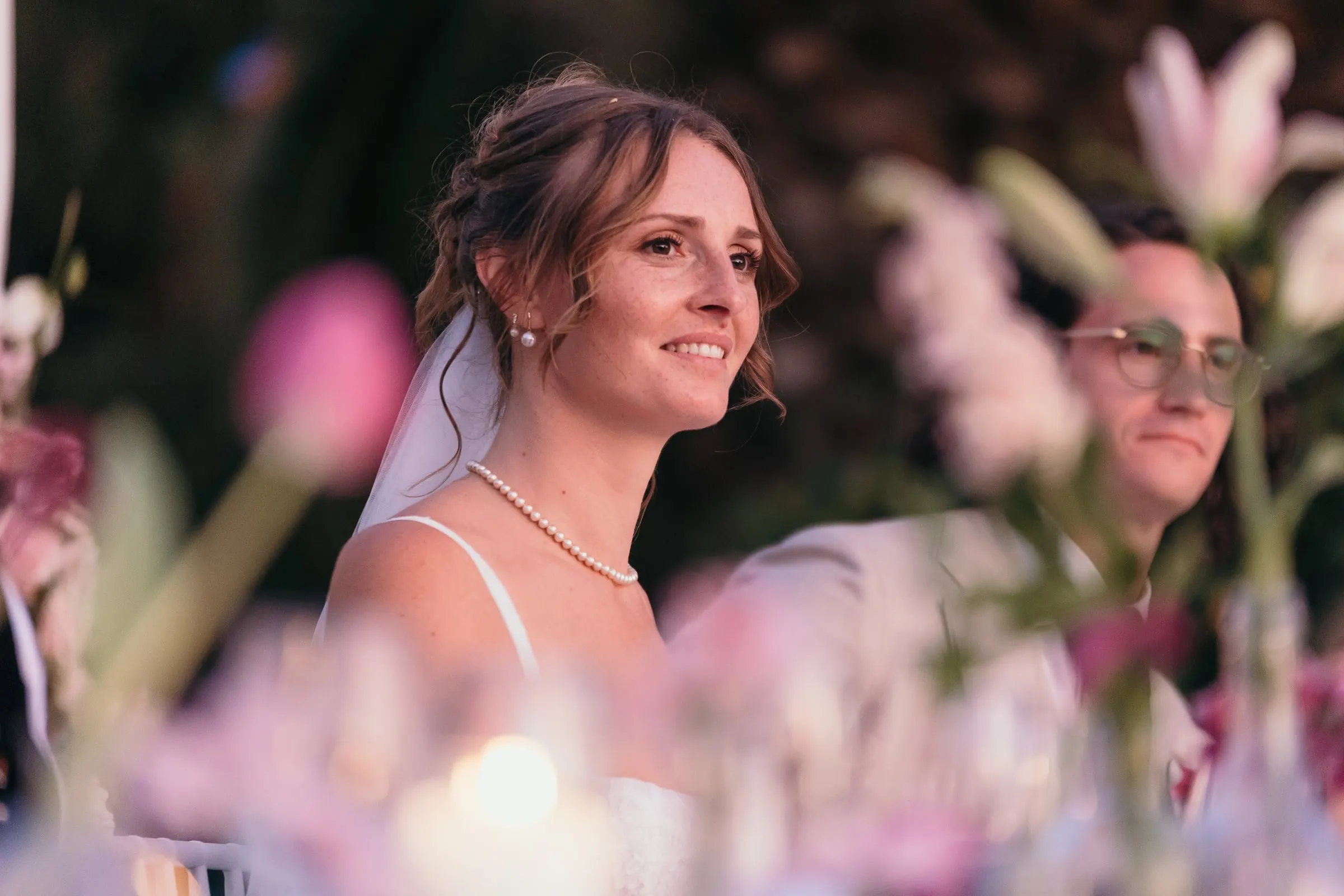 Bride smiling at the dinner table, seen through pink flowers and candles, at Hacienda San José, Mijas
