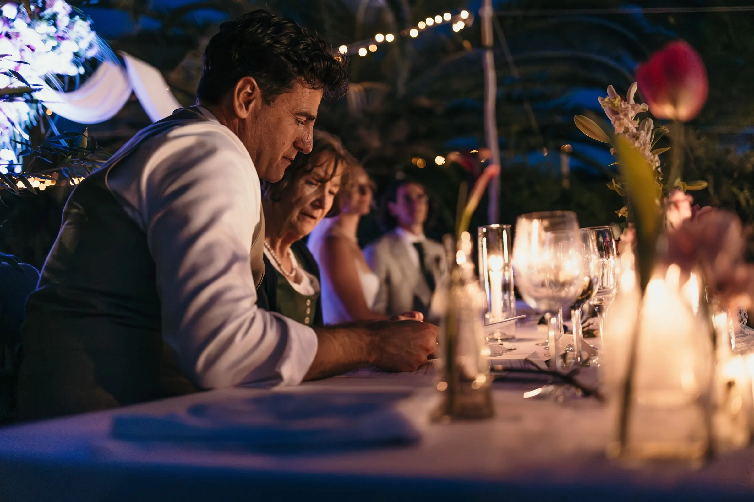 Guest in a grey suit reading from his notes at the candlelit dinner table at Hacienda San José, Mijas