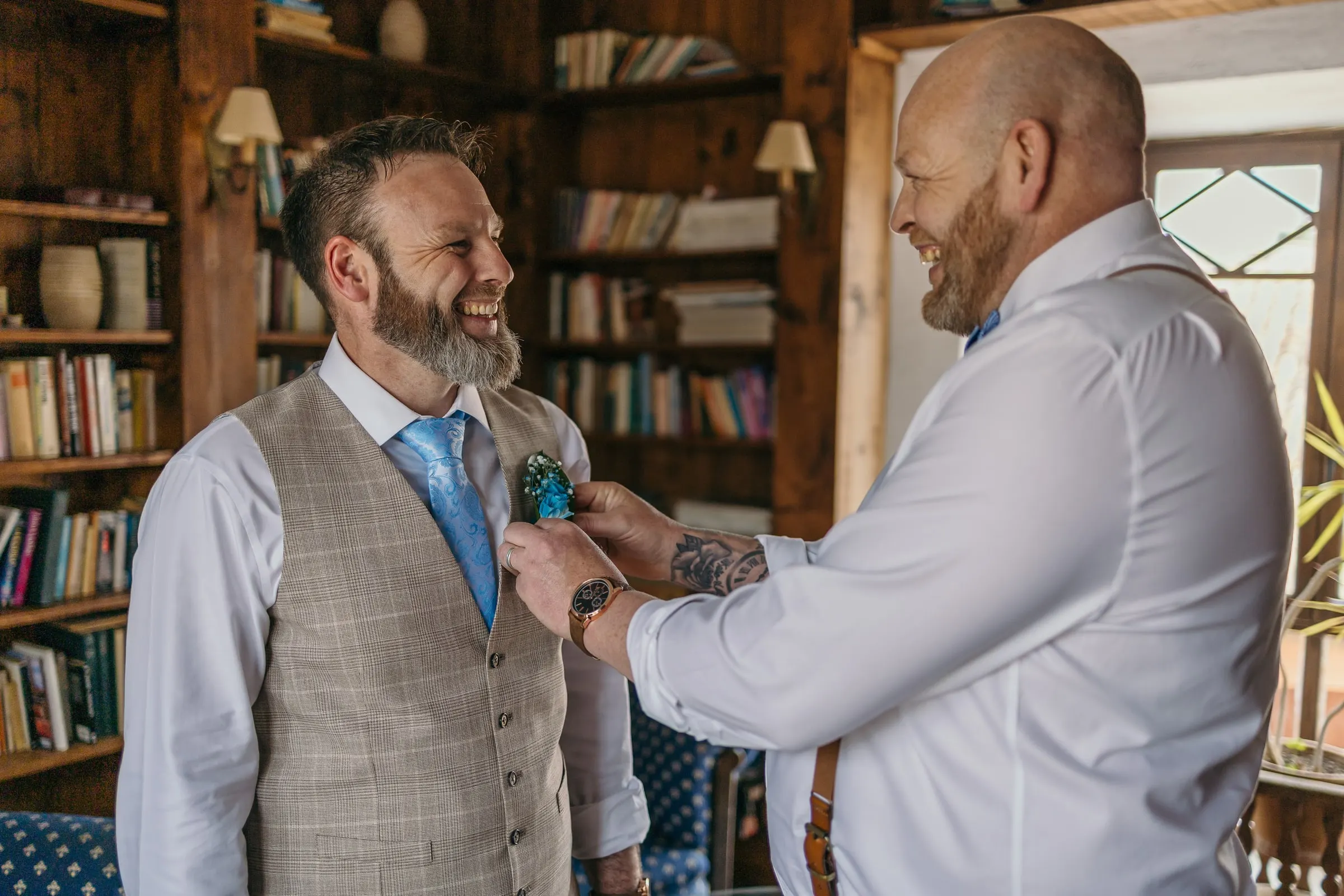Groomsman pinning the groom's buttonhole in the wood-panelled library at Hacienda San José