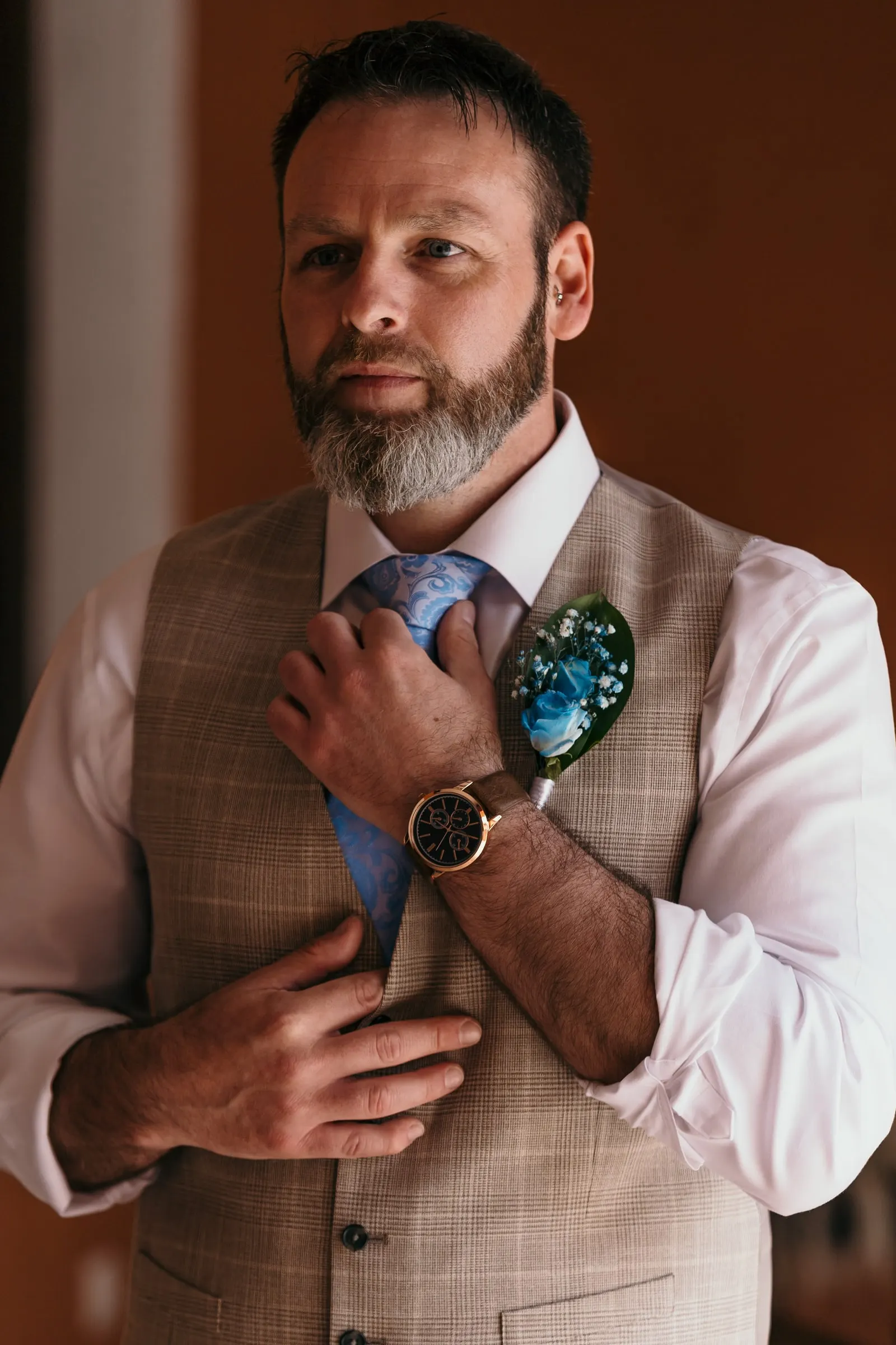 Groom adjusting his blue tie by the window, with a blue flower buttonhole, Mijas