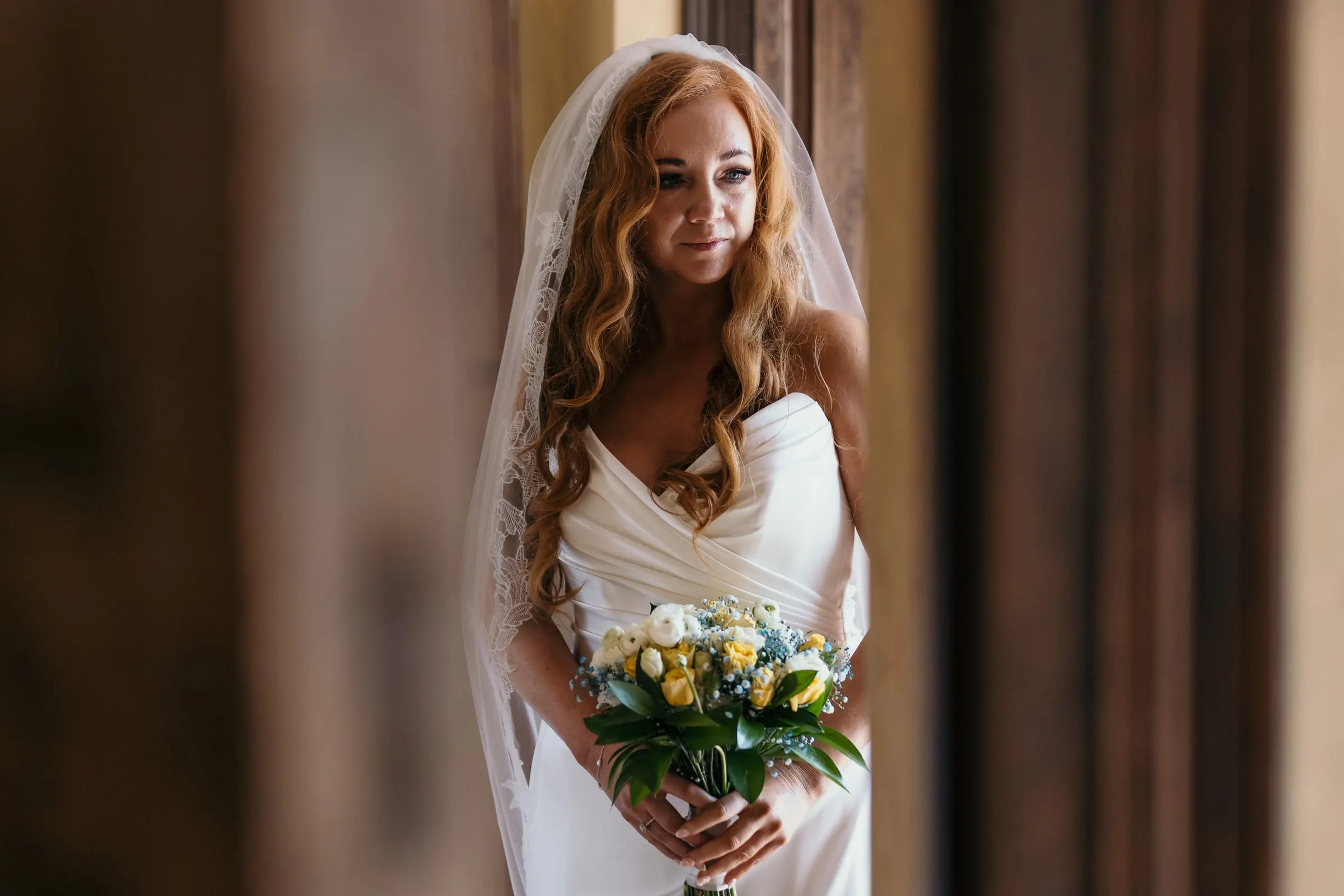 Bride looking down at her yellow and white bouquet, framed by a dark wooden door at Hacienda San José