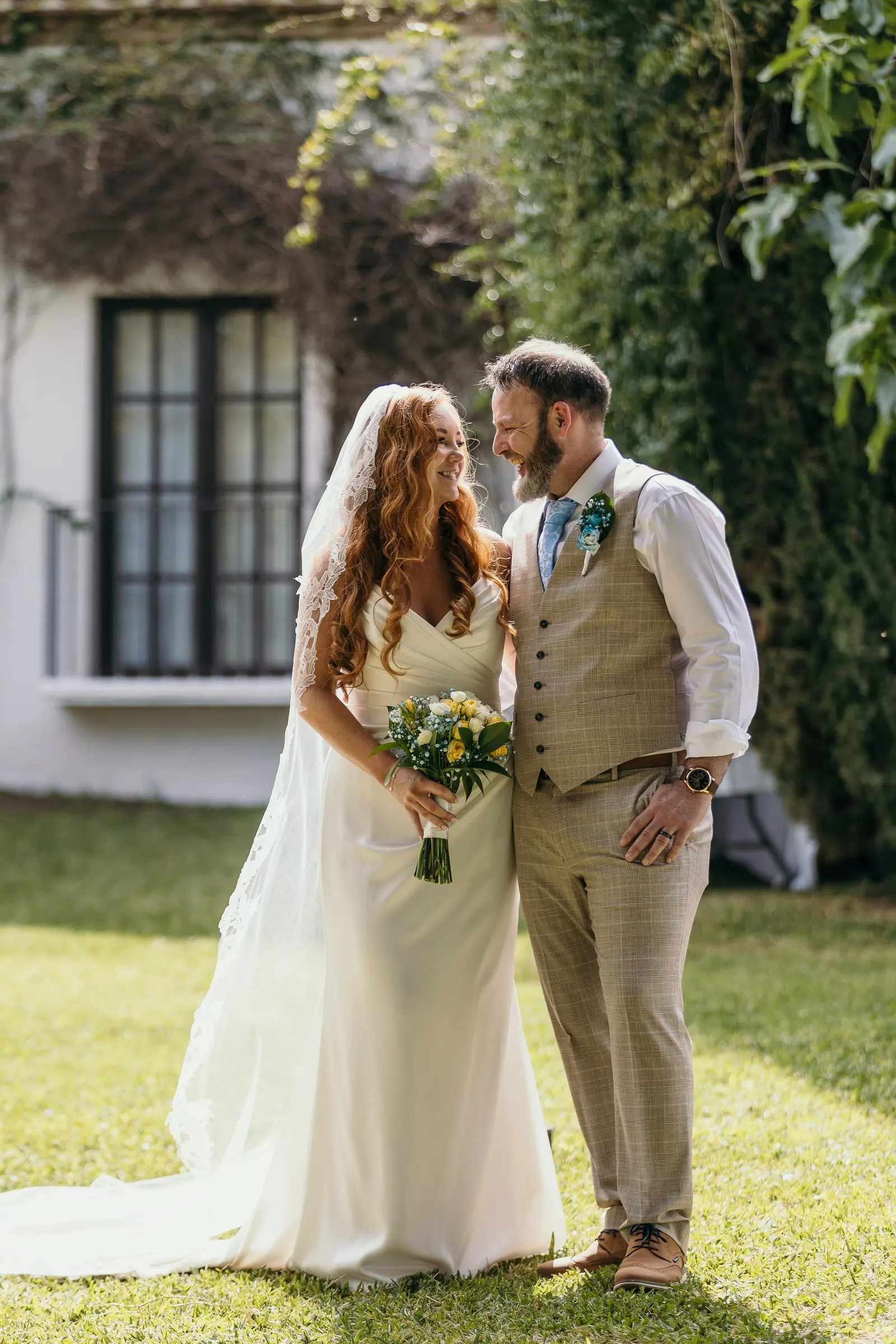 Bride and groom smiling at each other in front of an ivy-covered white cottage, Mijas