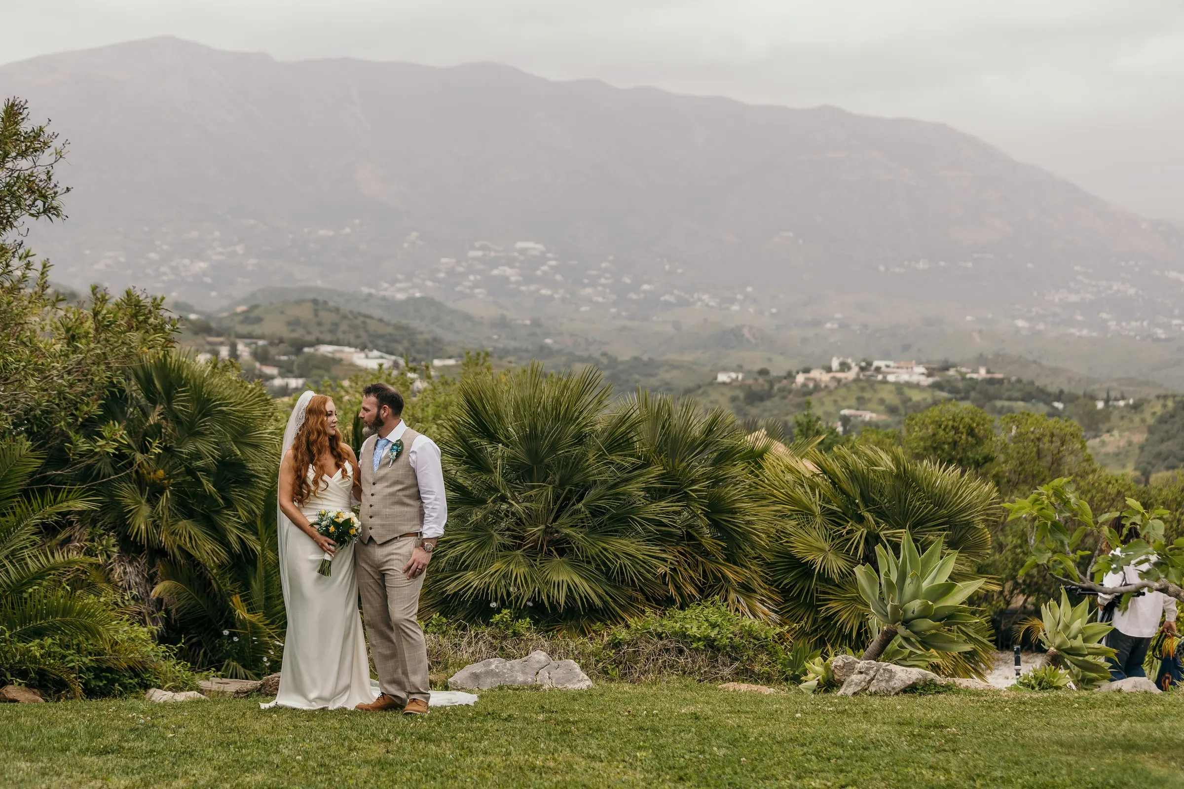 Bride and groom among fan palms on the lawn of Hacienda San José, with the Mijas mountains and white villages behind