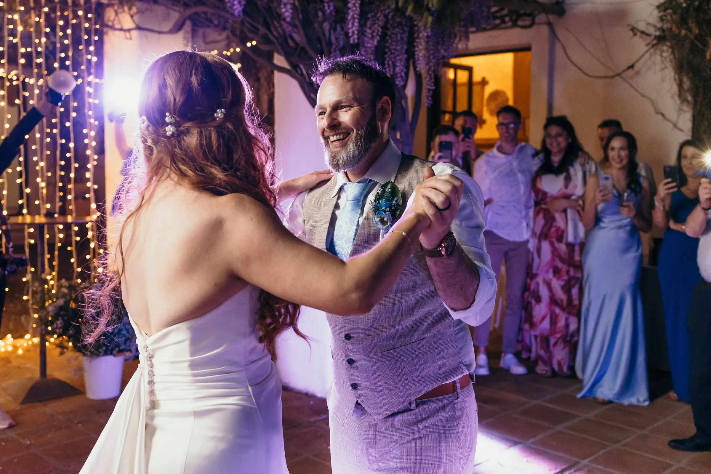 First dance in the courtyard lit in purple as guests film on their phones, Mijas