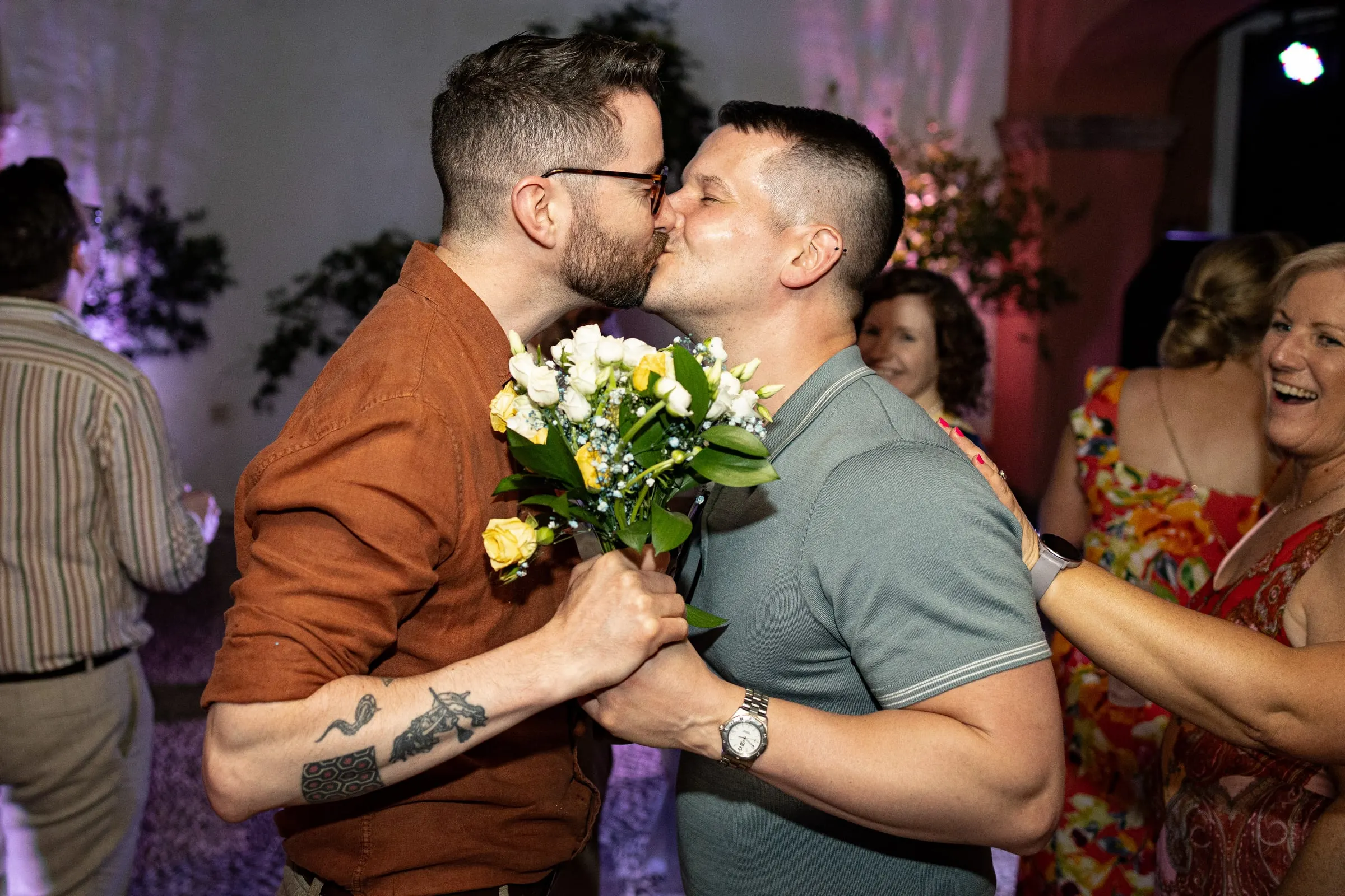 Two guests kissing on the dance floor holding the bride's bouquet, Mijas