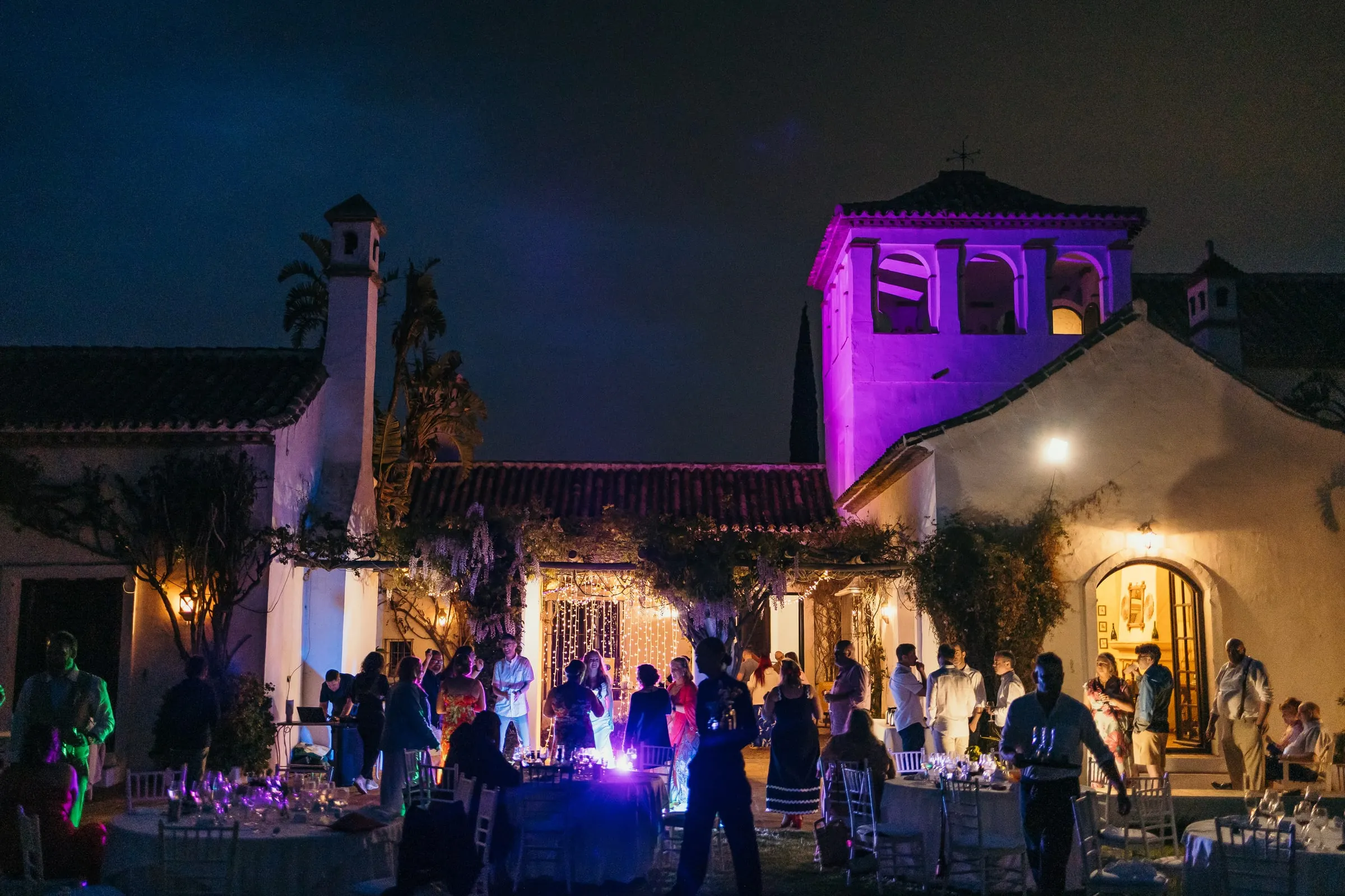The bell tower lit in violet above the evening party in the courtyard, Hacienda San José, Mijas