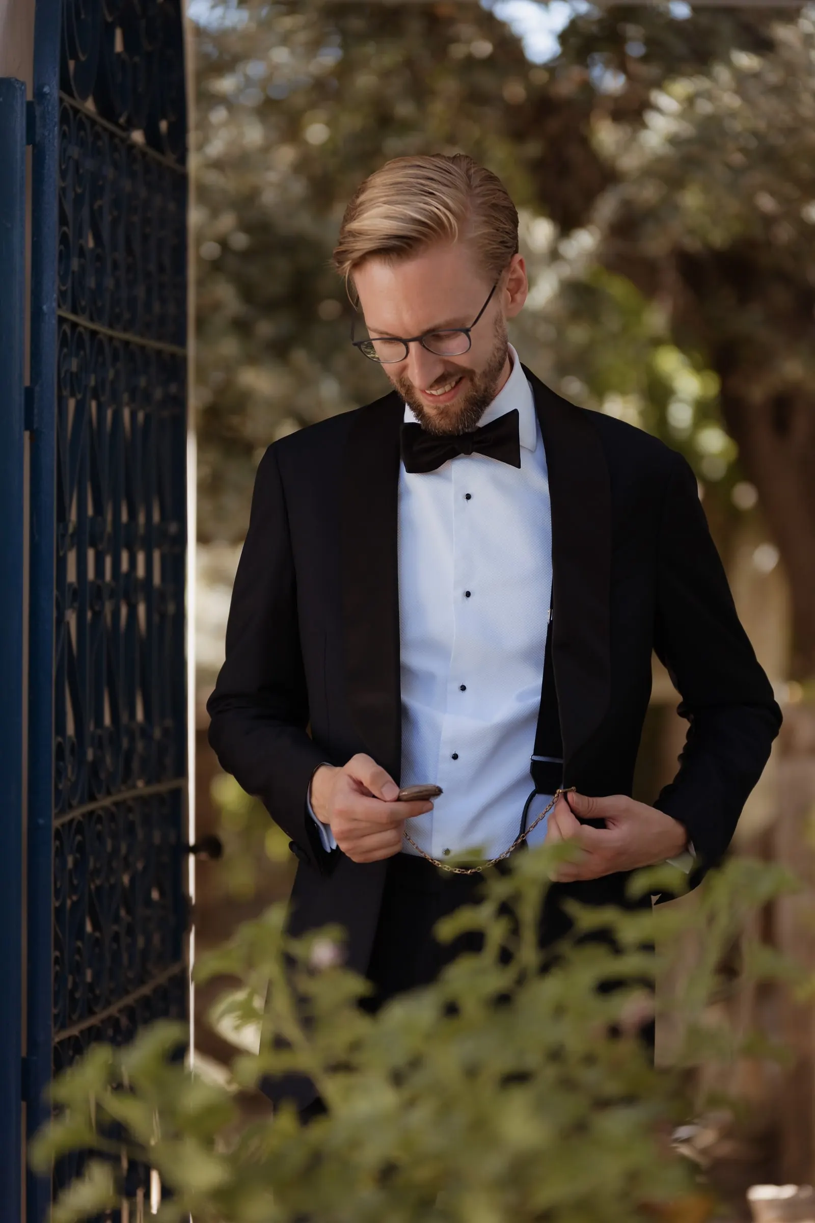 Groom in a tuxedo adjusting his cuff beside a blue iron gate at Los Pilares de Ronda
