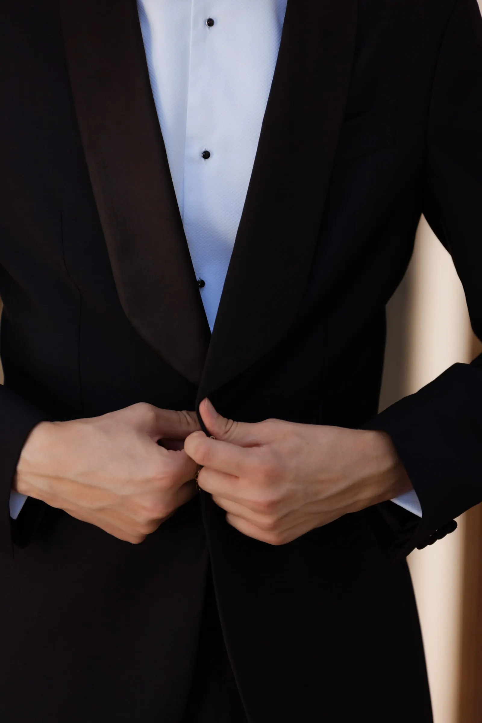 Close-up of the groom's hands buttoning his black tuxedo jacket