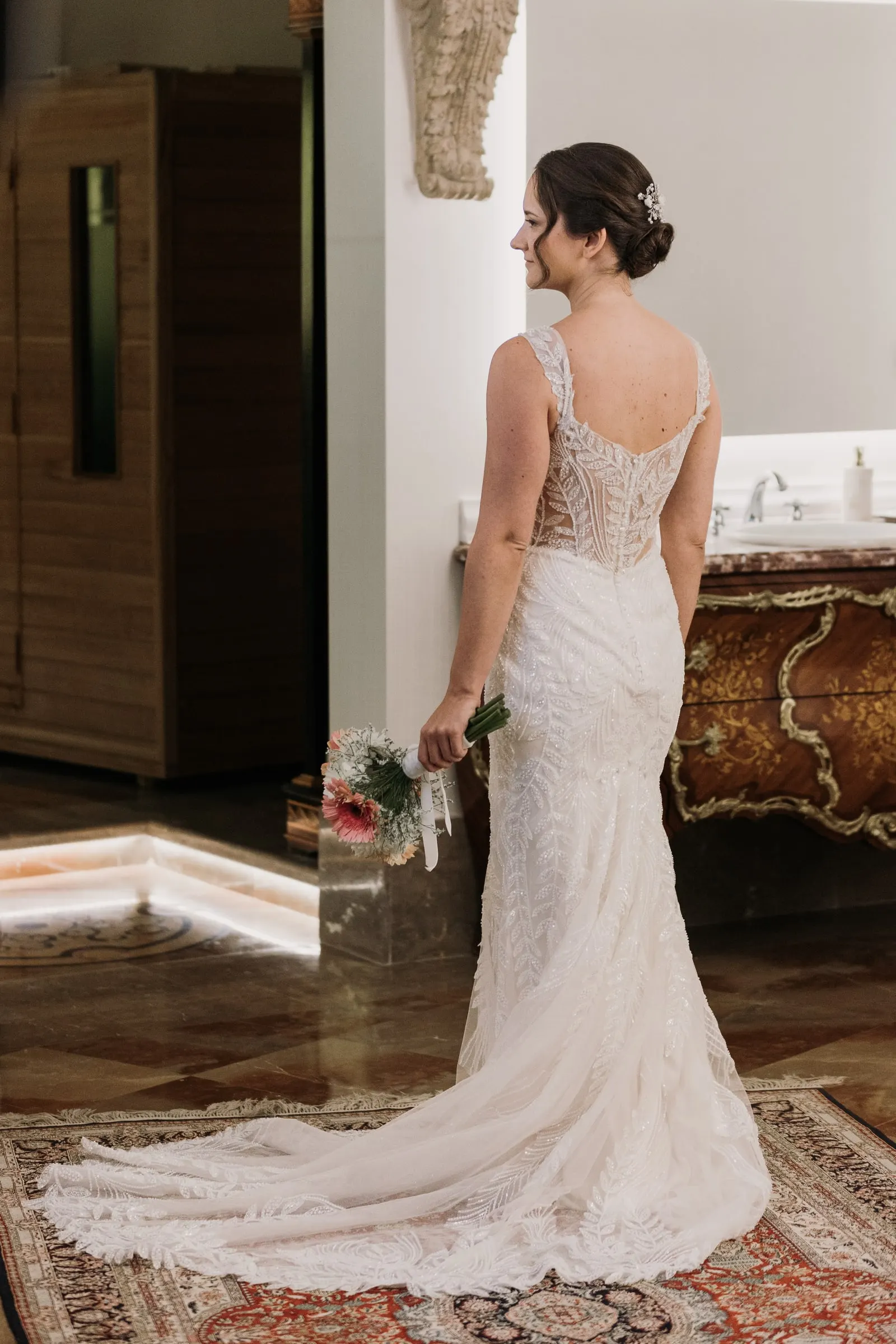 Bride from behind with her bouquet and long train on a Persian rug