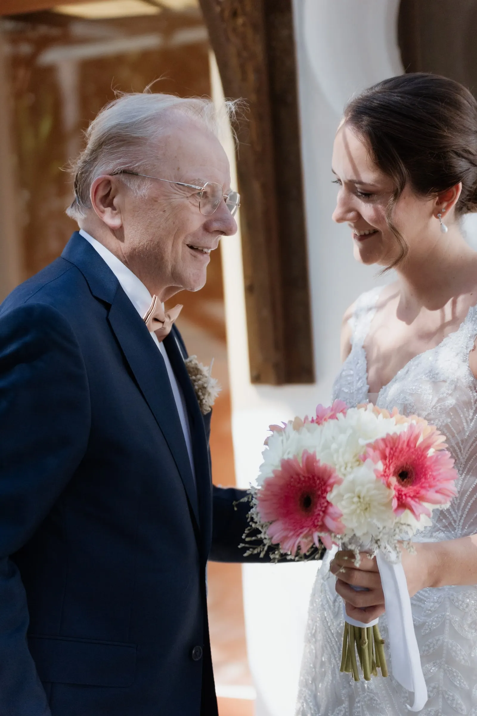 Bride laughing with her older relative, holding a bouquet of pink gerberas