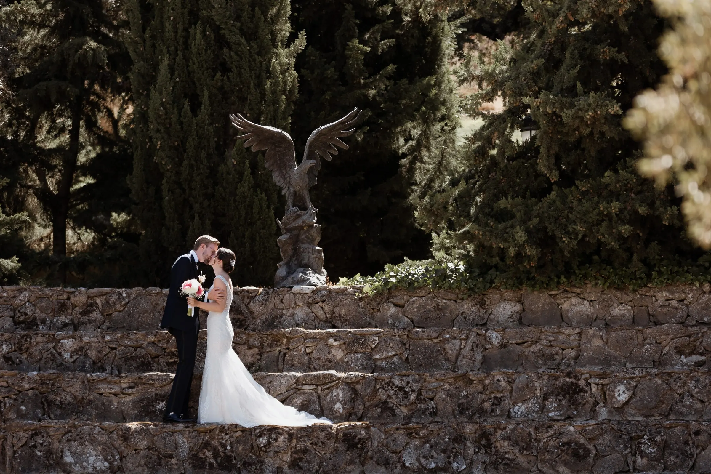 Couple kissing on the stone steps with the bronze eagle and cypresses behind