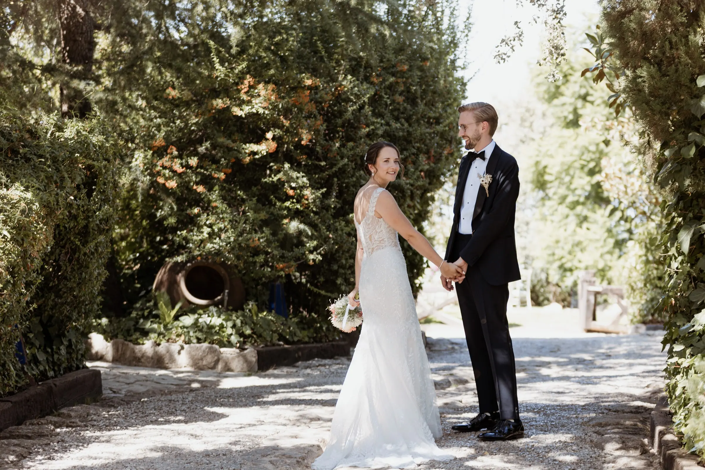 Bride and groom holding hands on a gravel path under a canopy of trees