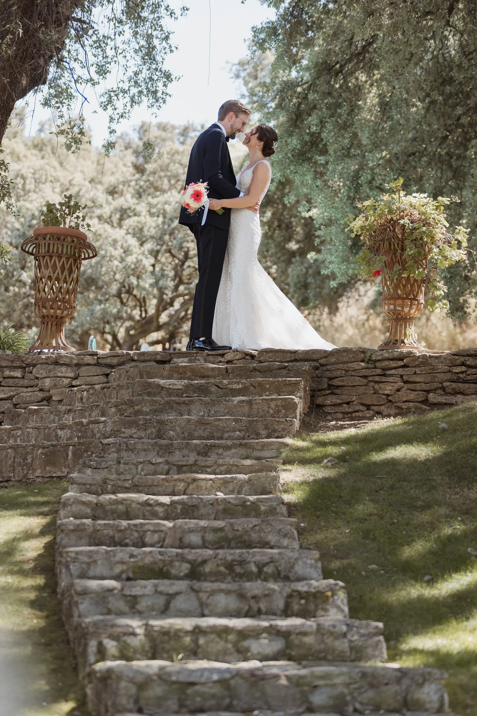 Couple kissing at the top of old stone steps between flower urns under an oak