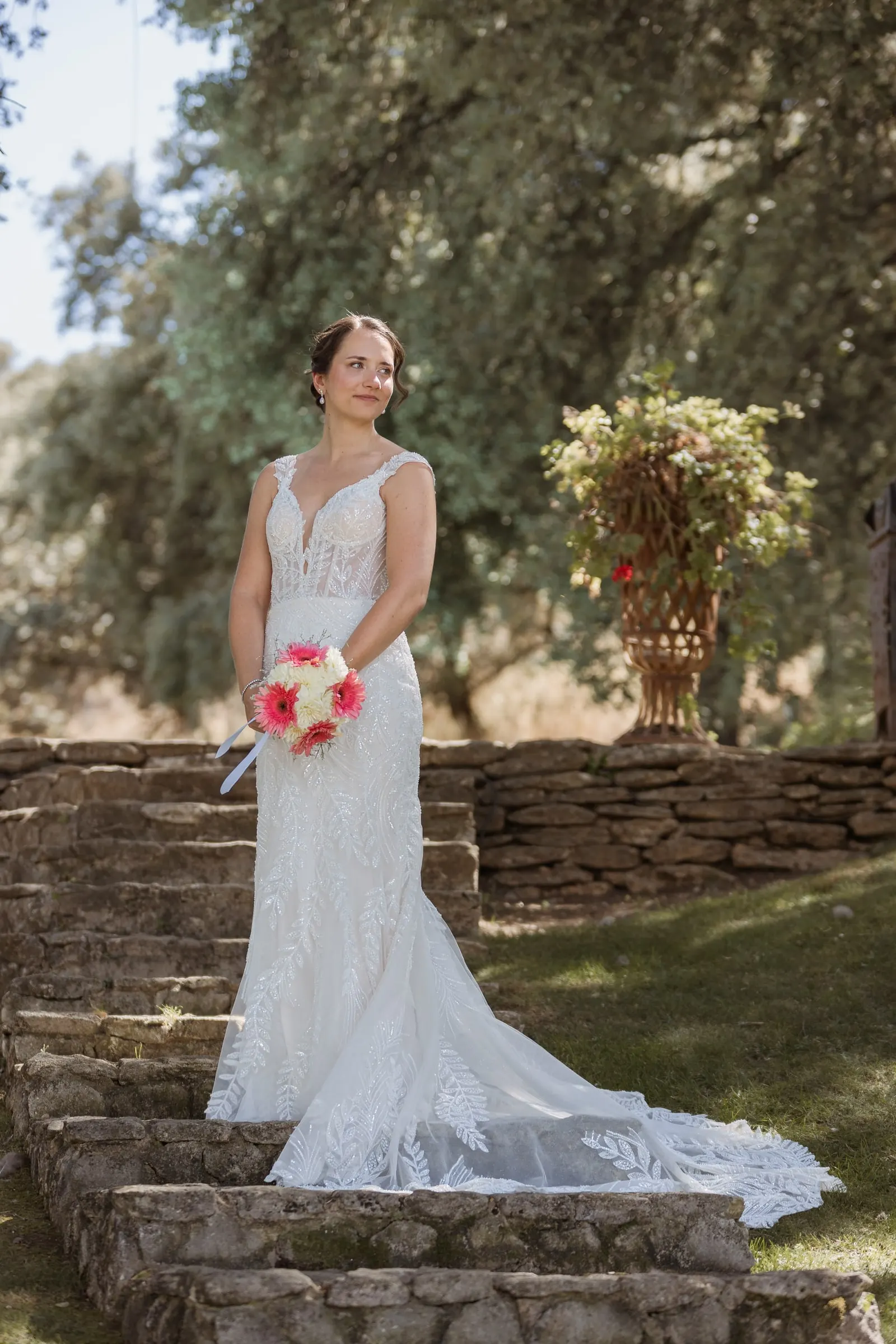 Bride holding her pink bouquet on the stone steps beside a flower urn at Los Pilares de Ronda