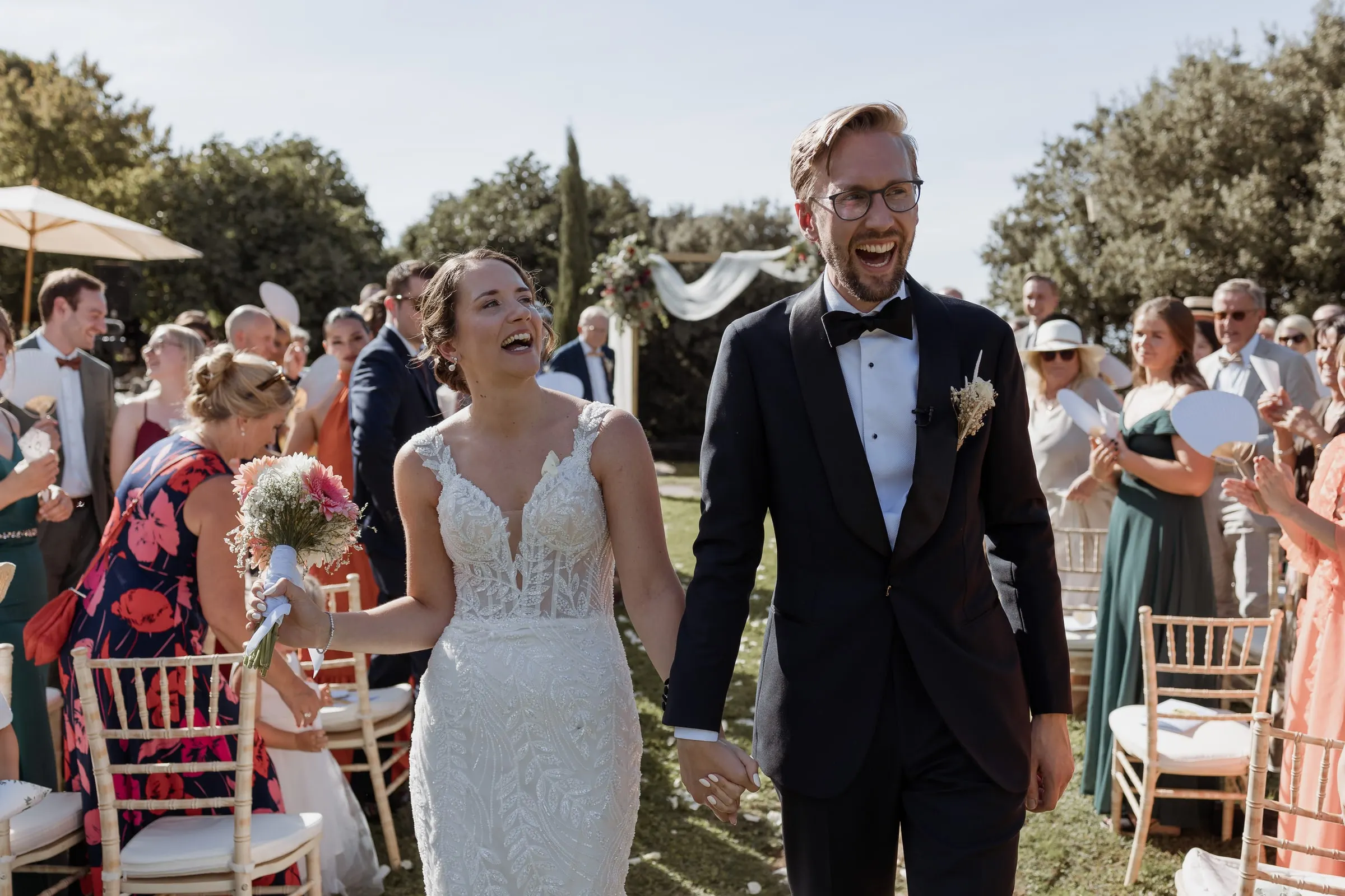 Bride and groom laughing as they leave the ceremony among their guests