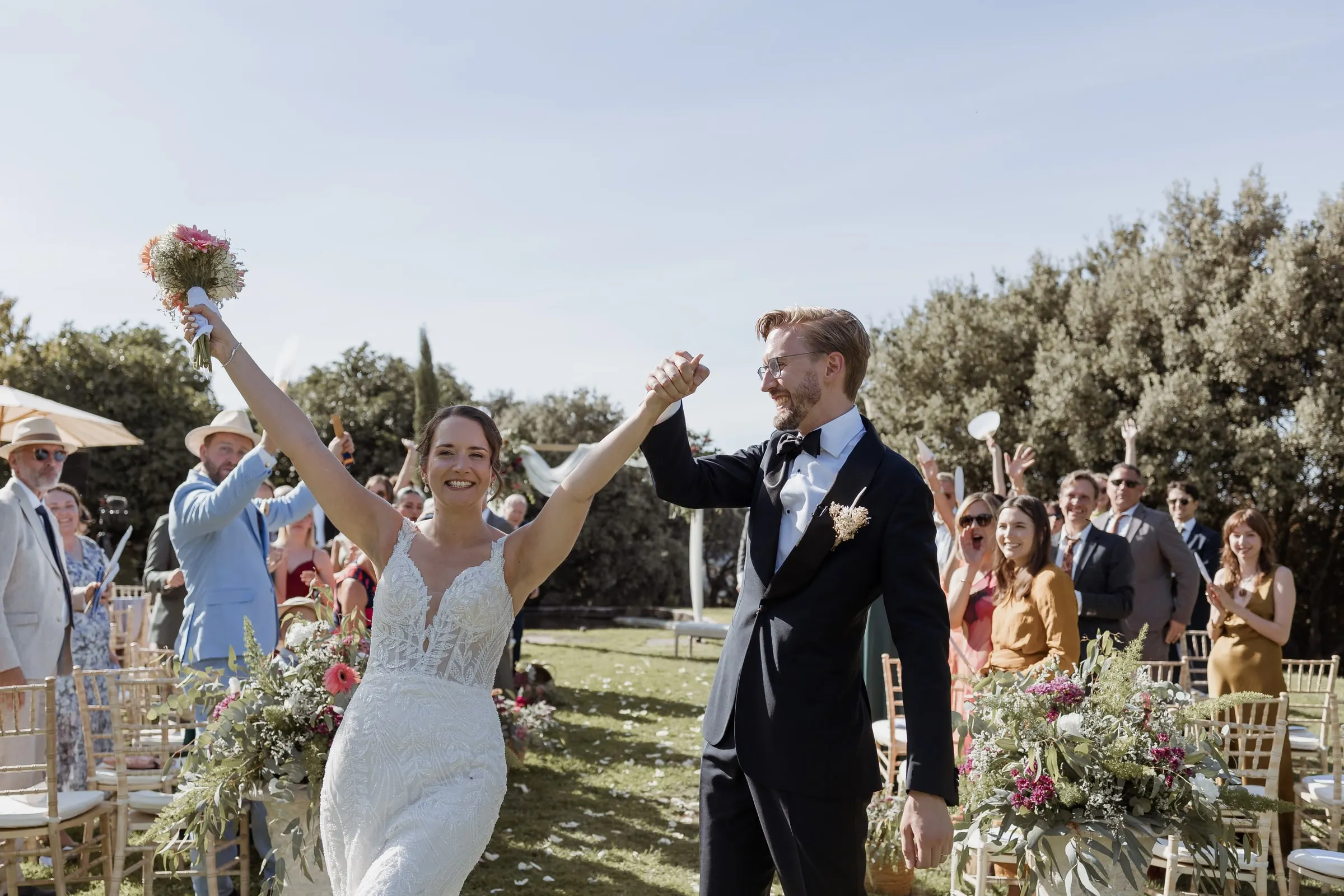 Bride raising her bouquet in triumph at the end of the aisle