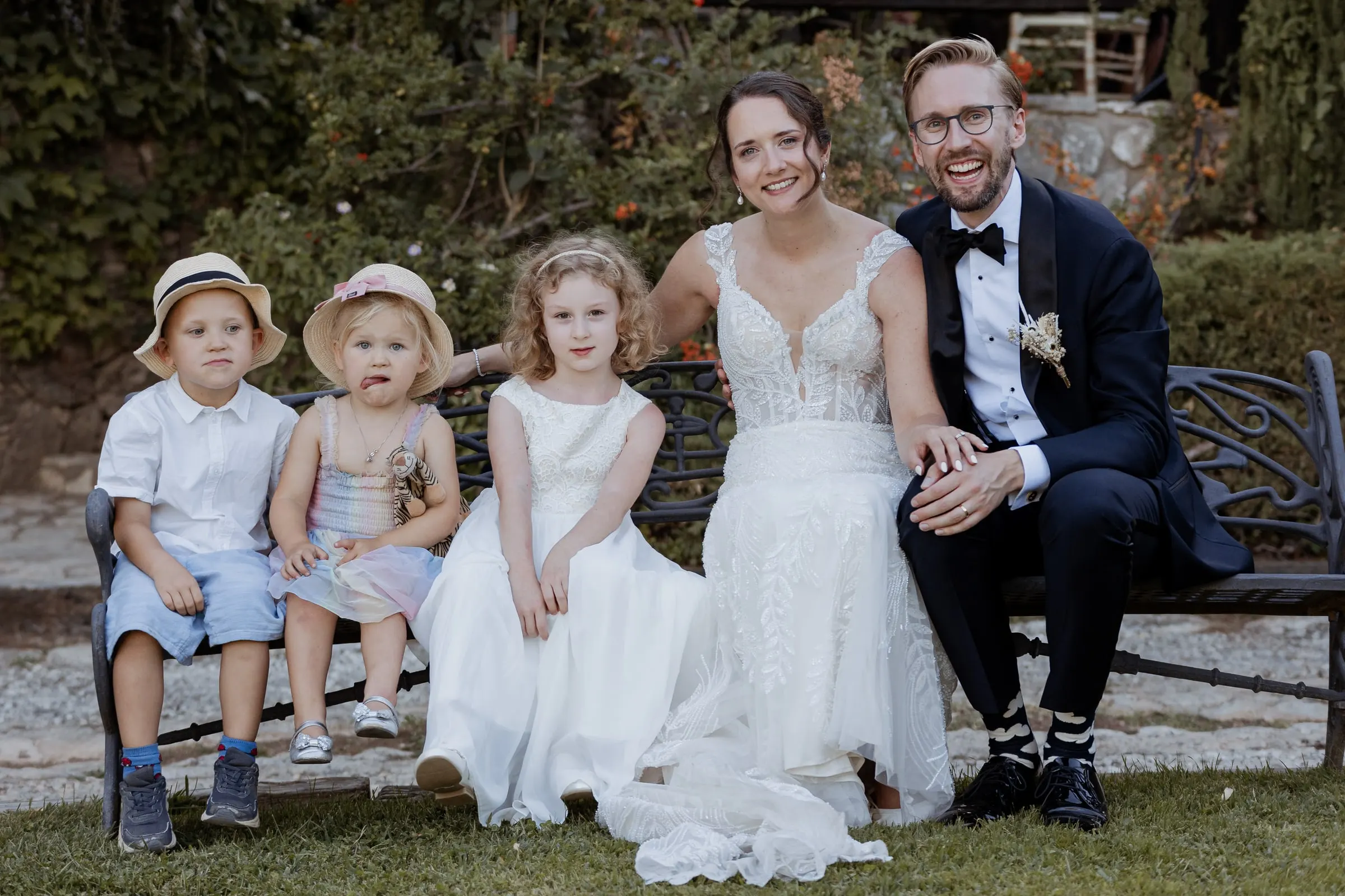 Bride and groom on a garden bench with the page boy and flower girls