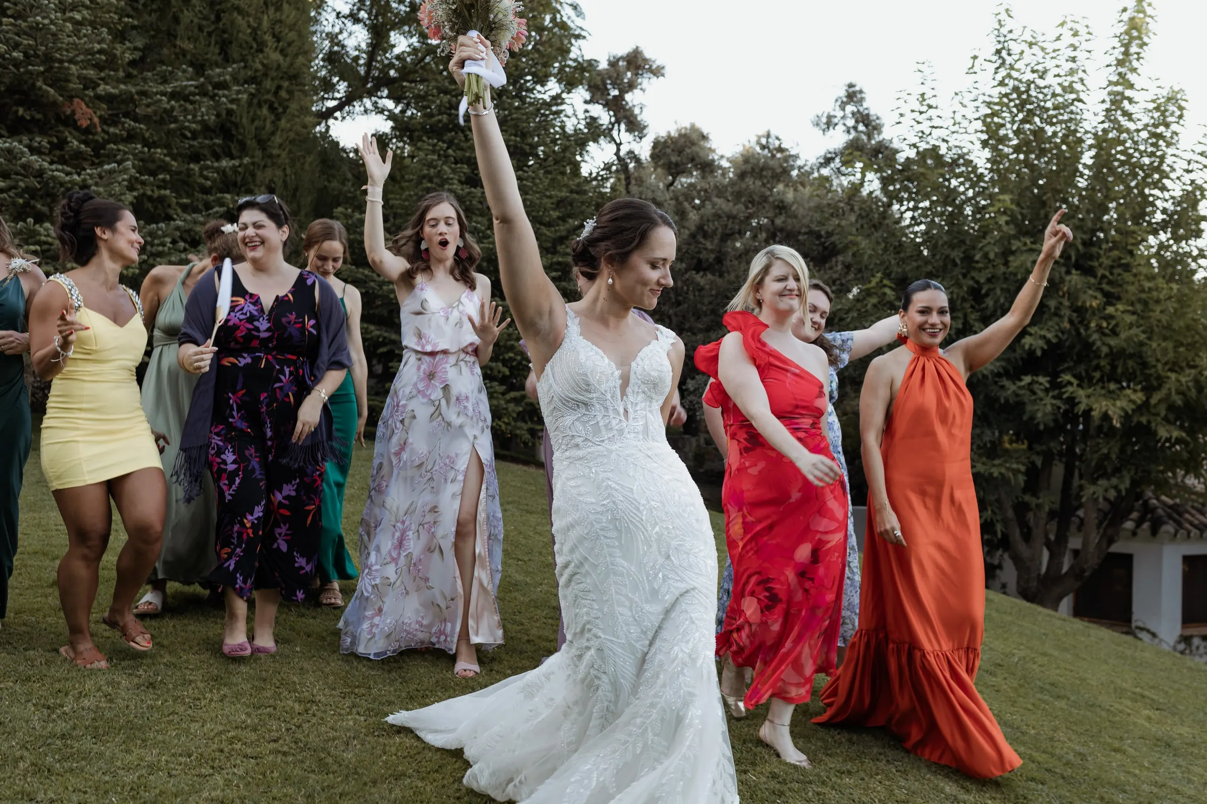 Bride dancing on the lawn with her friends in colourful dresses