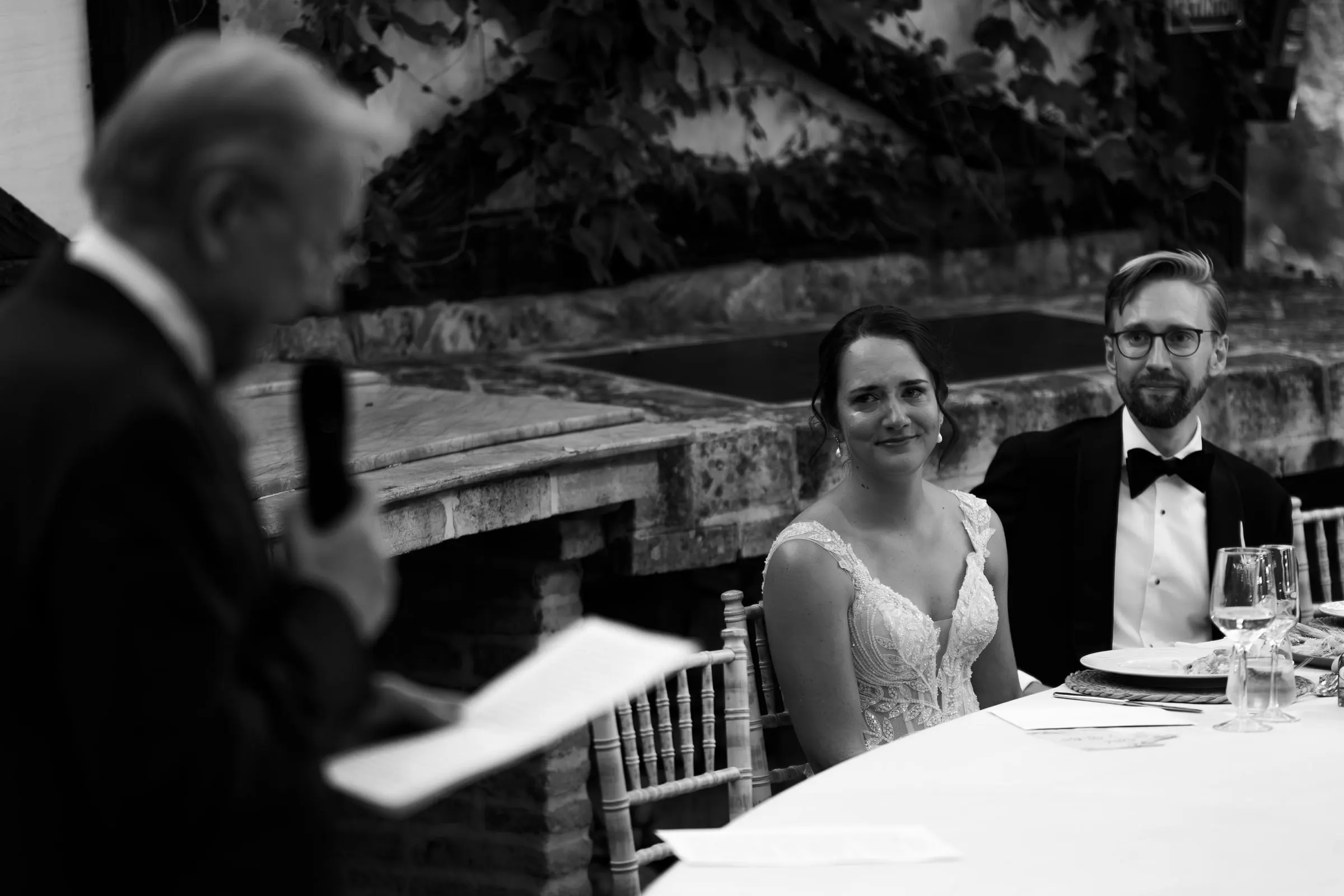 Black and white photo of a family speech as the couple listens at the table