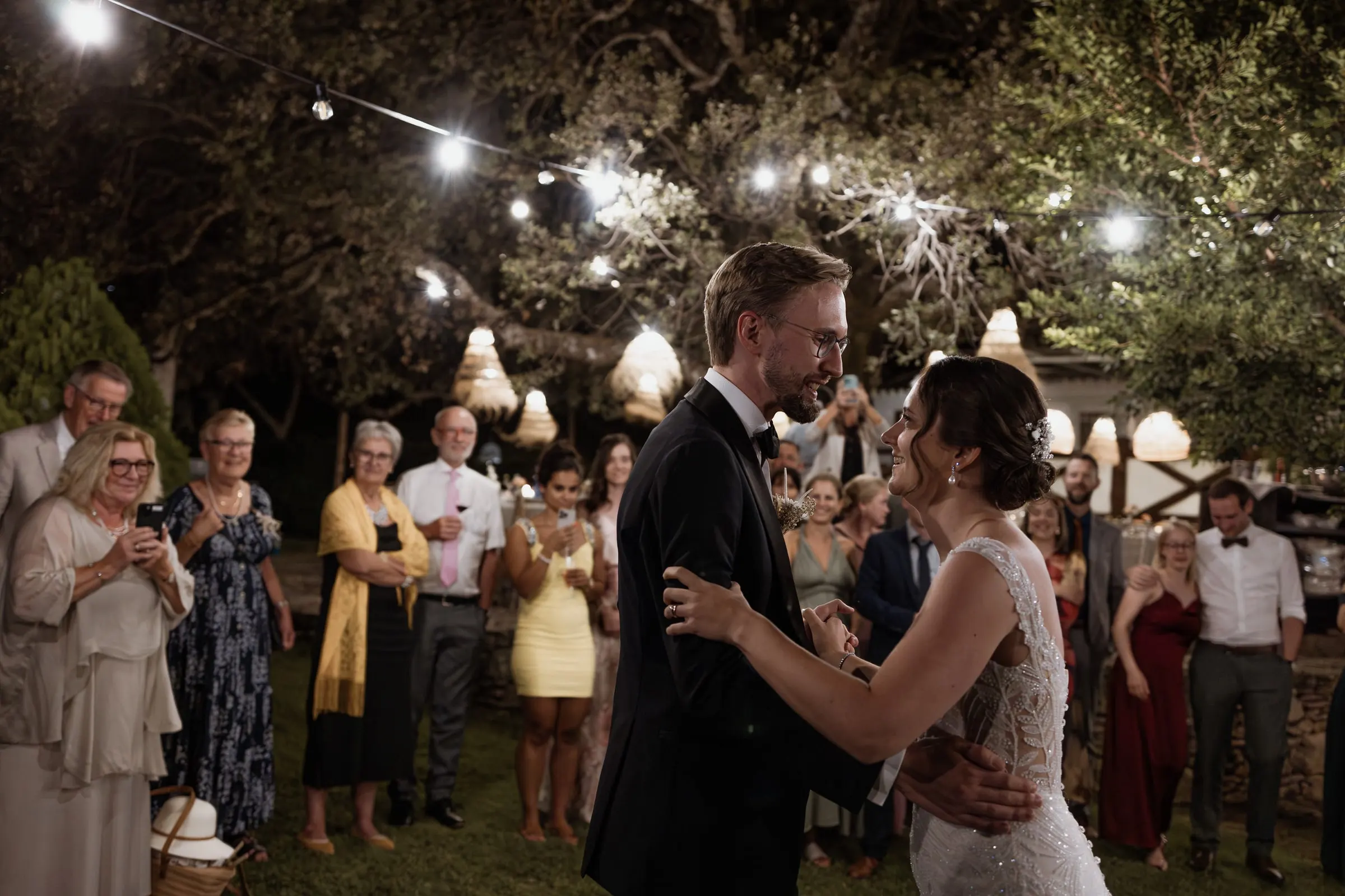 Couple dancing surrounded by guests under the trees at night